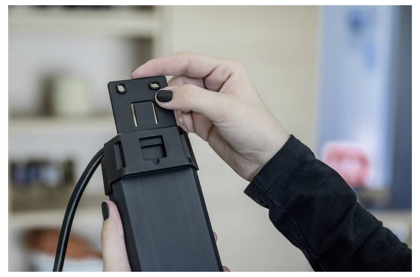 Nahaufnahme einer Person, die ein schwarzes Gerät oder ein Gerätezubehörteil mit einem Kabel mit beiden Händen anpasst und im Inneren hält.