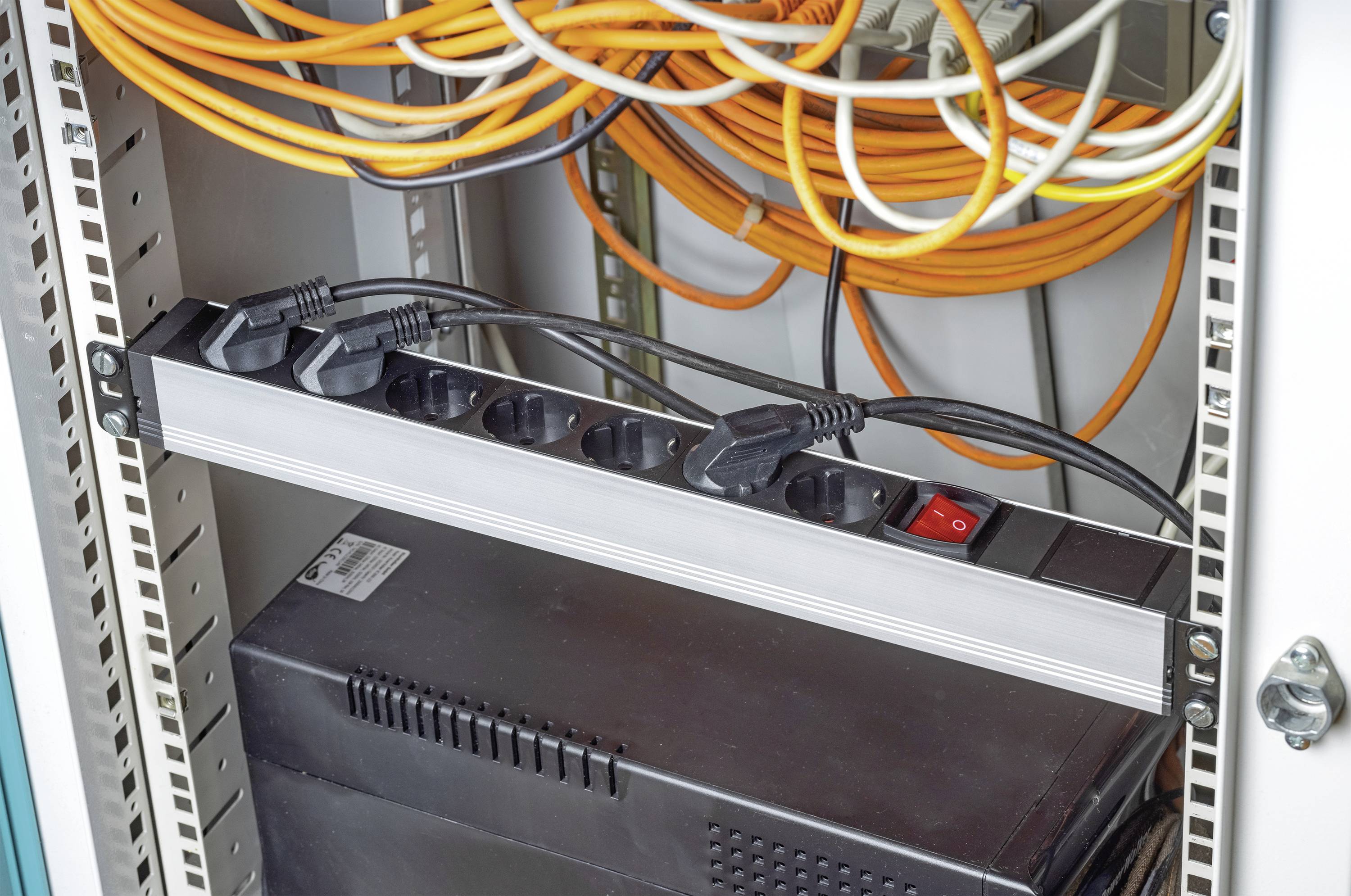 Ein offener Serverschrank mit einer Steckdosenleiste, mehreren verbundenen Kabeln und einem Gerät darunter.