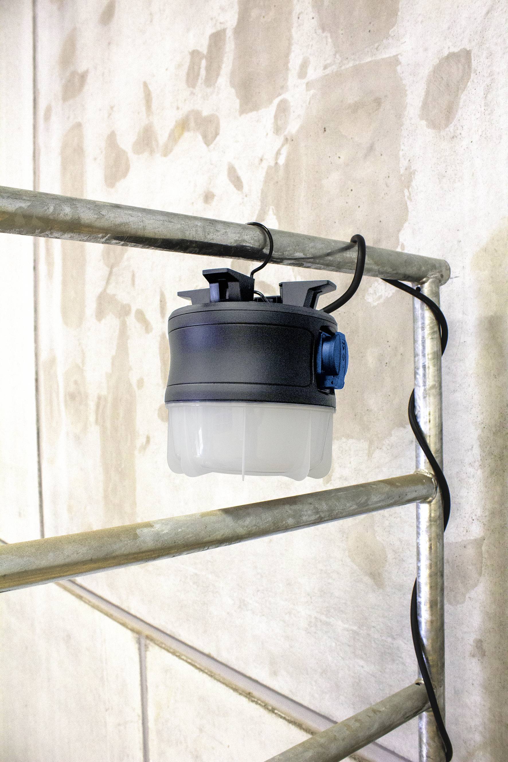 Eine runde, tragbare Lampe, befestigt an einem Metallgestell an einer Betonwand, mit sichtbarem Kabel für Stromversorgung.