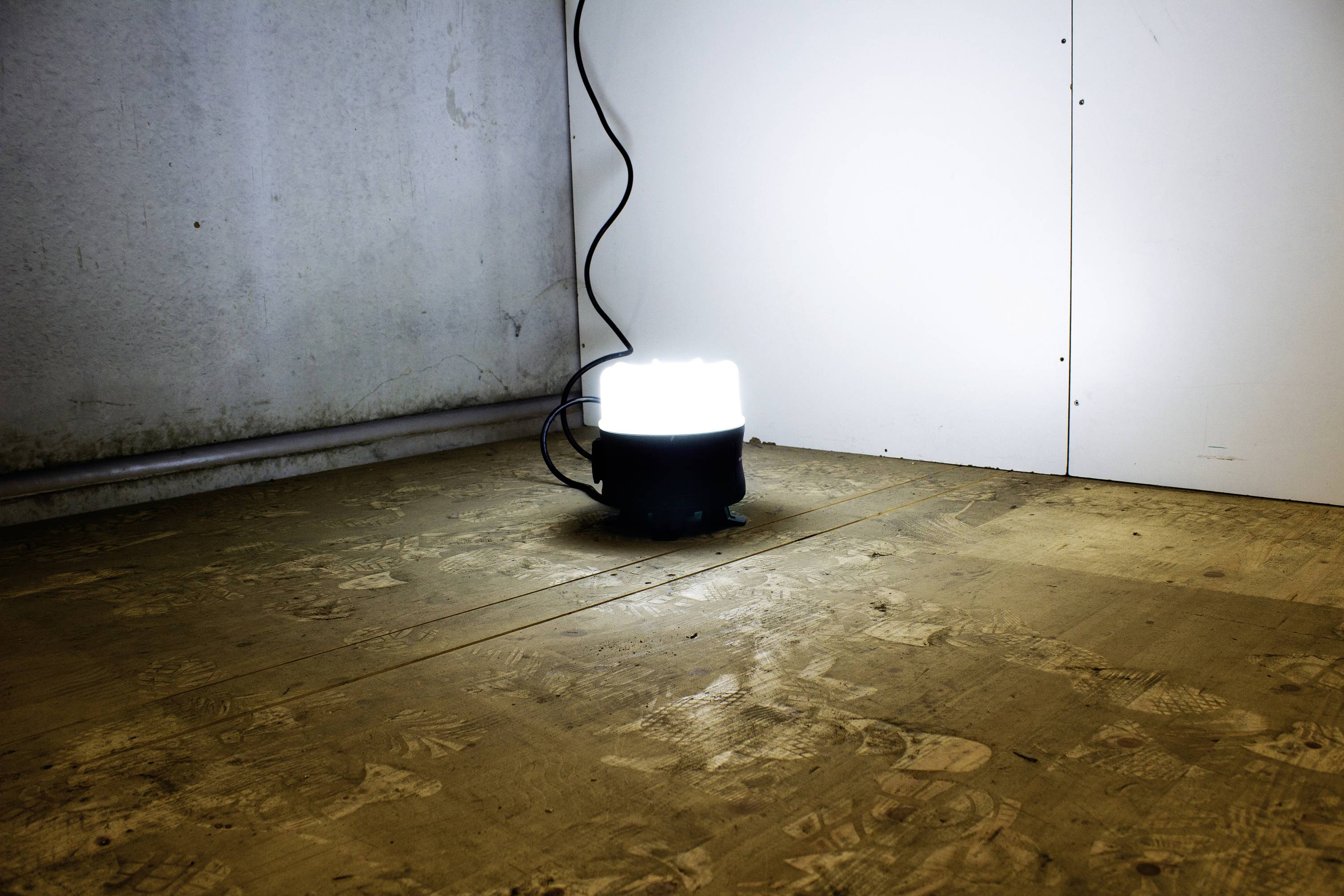 Eine Lampe auf dem Boden in einer spärlich beleuchteten Ecke eines Raumes. Die Lampe strahlt hell nach oben und erhellt den Bereich.