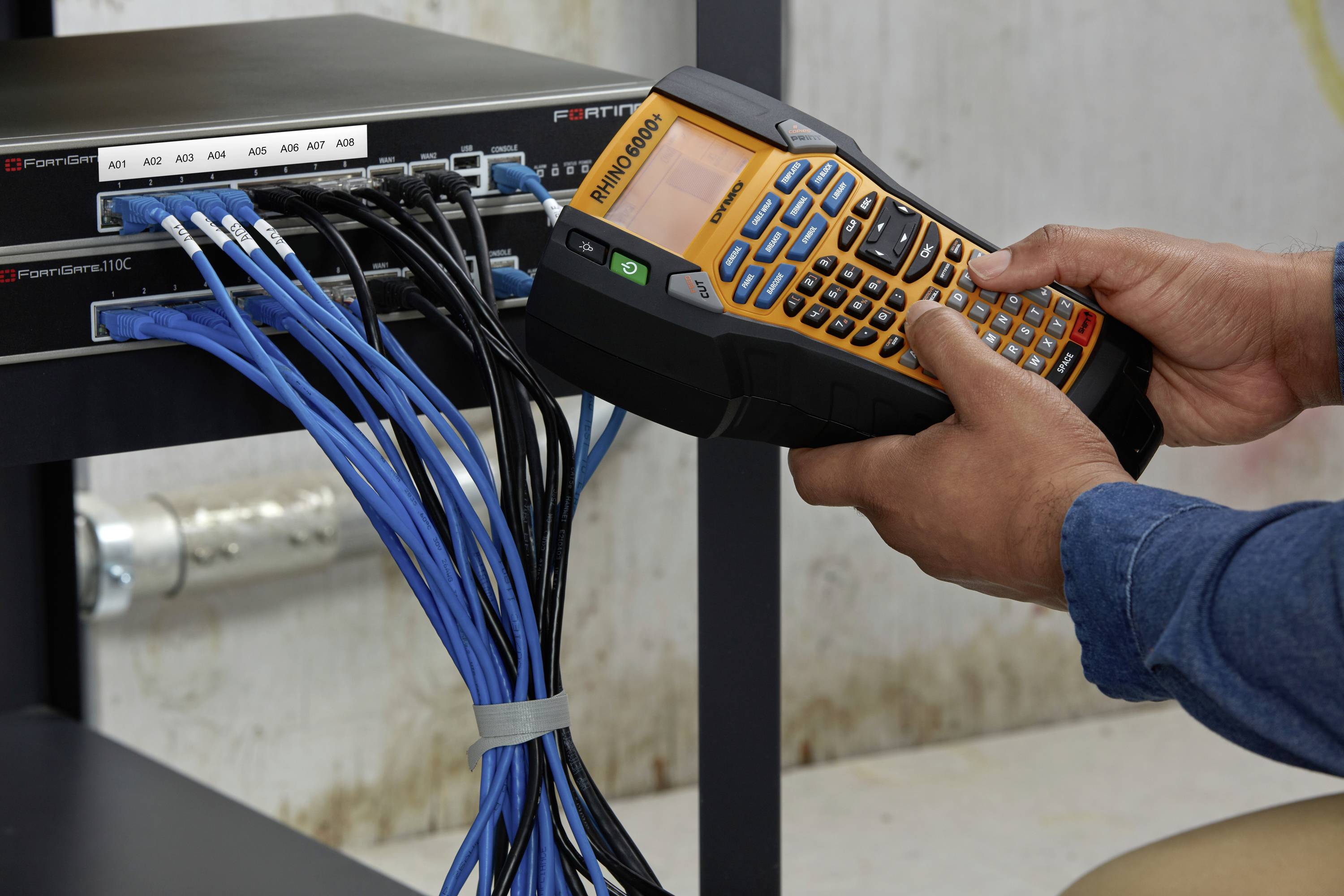 Eine Person benutzt ein tragbares Messgerät, um Kabel an einem Netzwerk-Switch zu überprüfen, der an einem Regal montiert ist.