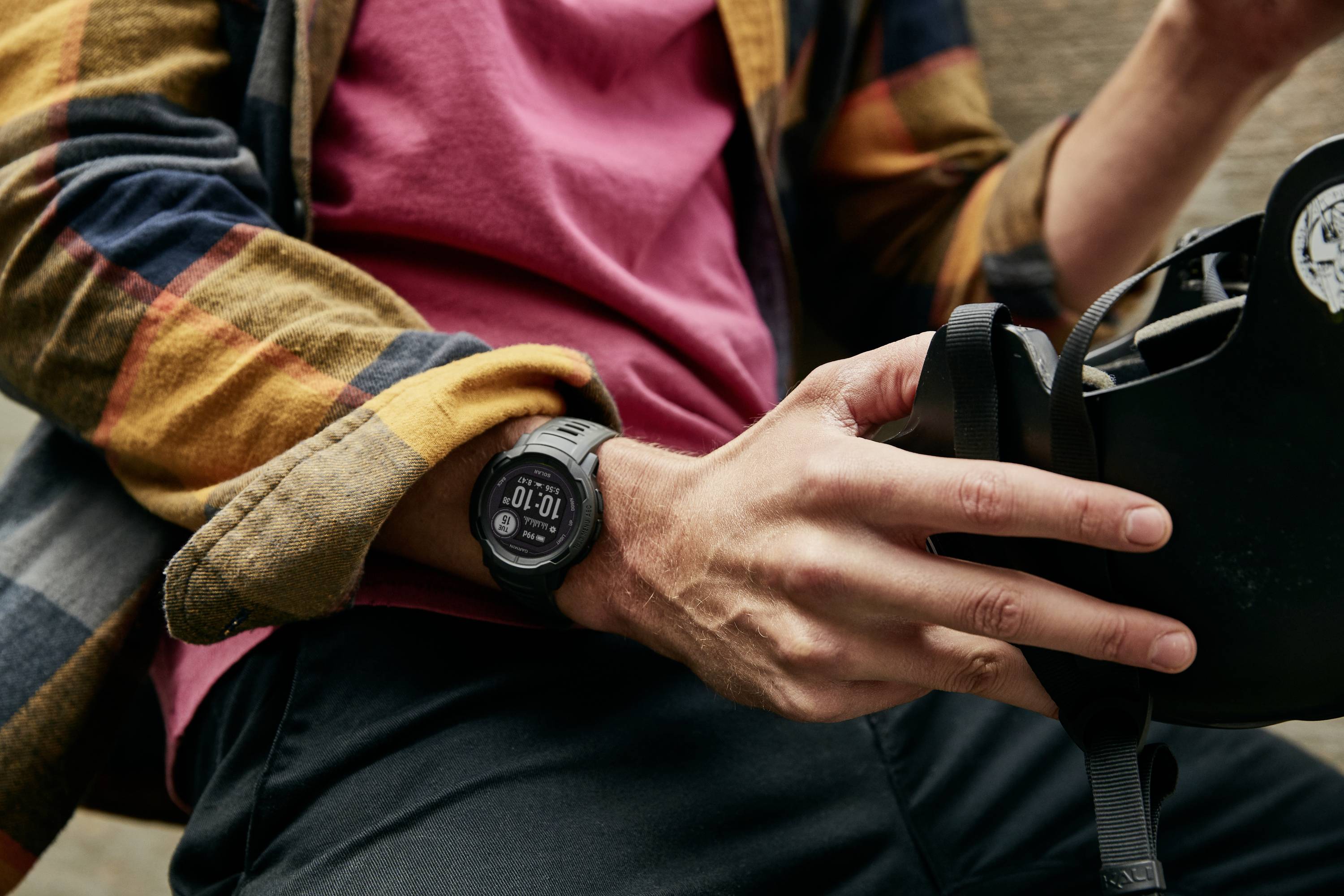 Eine Person hält einen schwarzen Helm und trägt eine Uhr mit digitaler Anzeige am Handgelenk. Der Fokus liegt auf den Händen und der Uhr.