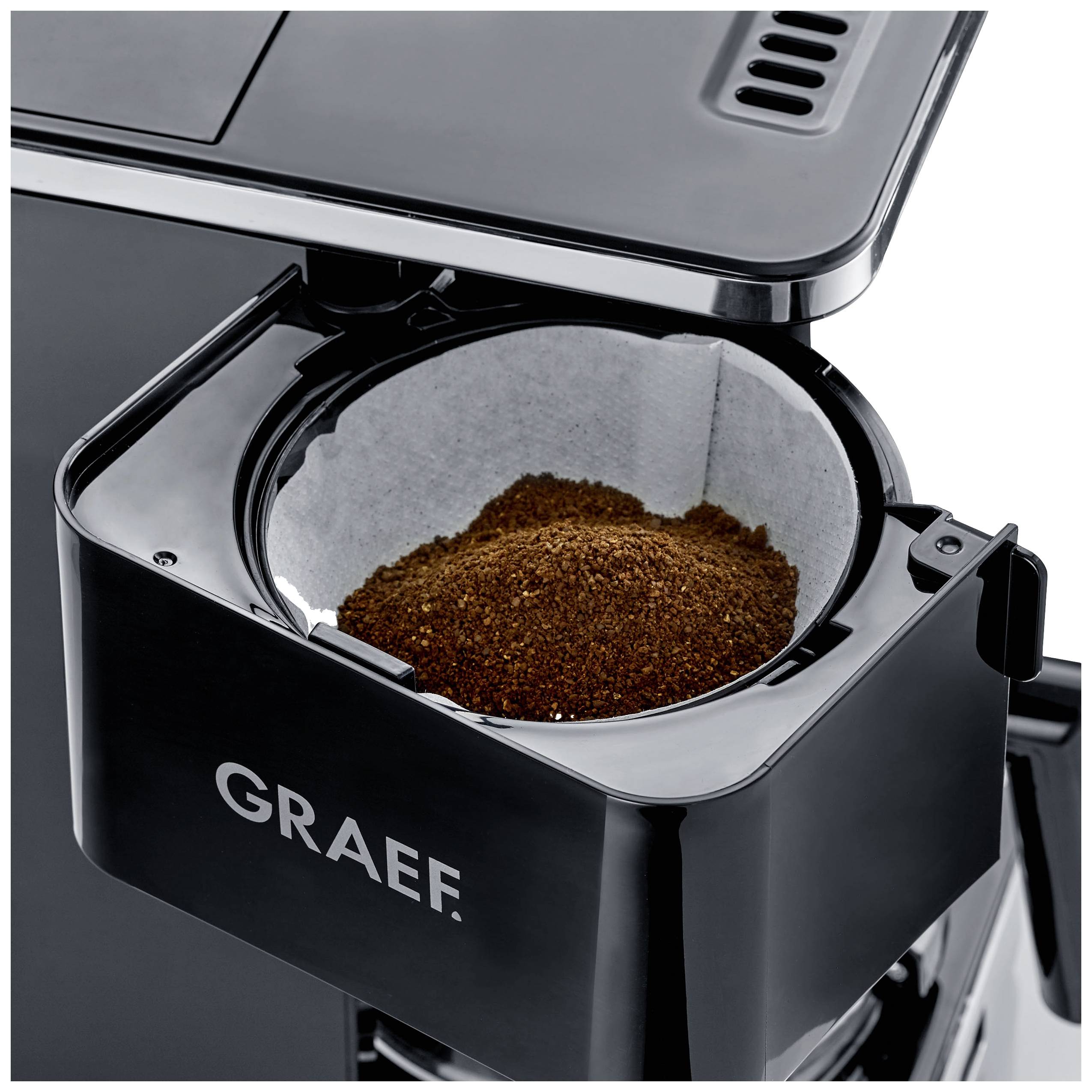 Filterkaffeemaschine mit geöffnetem Kaffeefilterfach, gefüllt mit gemahlenem Kaffee. Markenname 'Graef' sichtbar auf der Maschine.