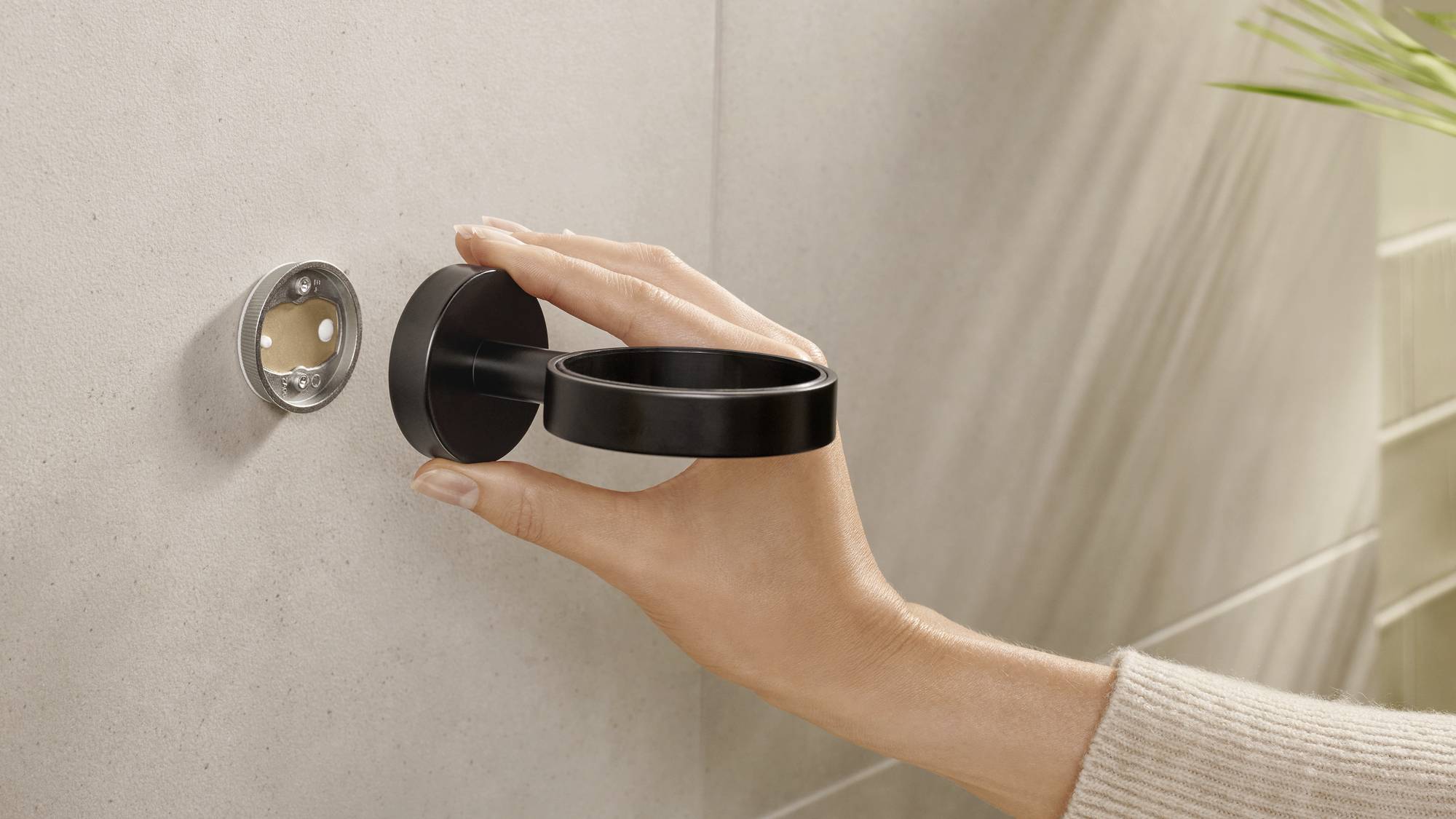 Eine Hand befestigt einen runden, schwarzen Türgriff an einer grauen Wand.