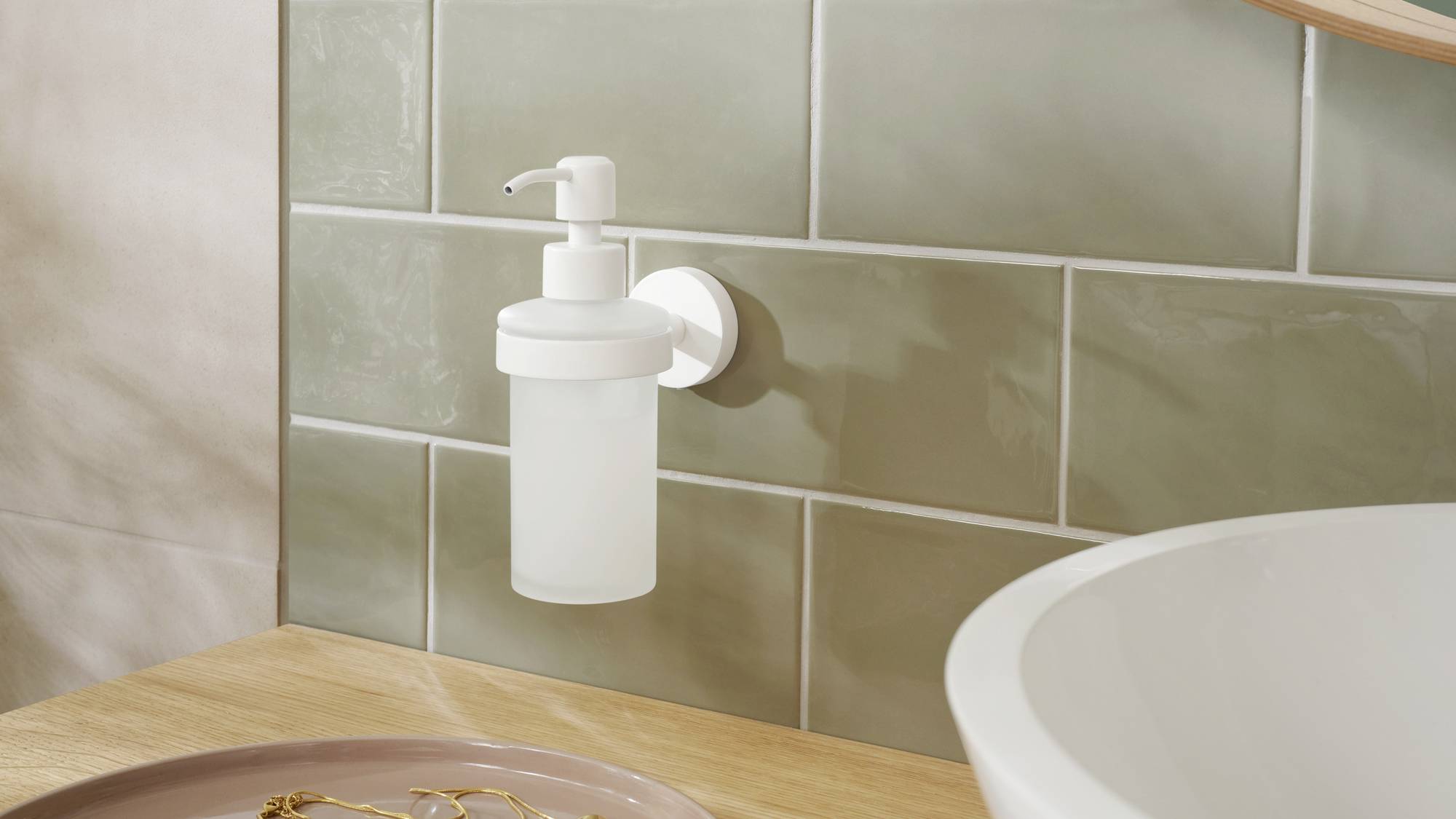 Ein schlichter, weißer Seifenspender ist an einer Wand mit grünen Fliesen angebracht, neben einer hölzernen Arbeitsfläche und einem Waschbecken.