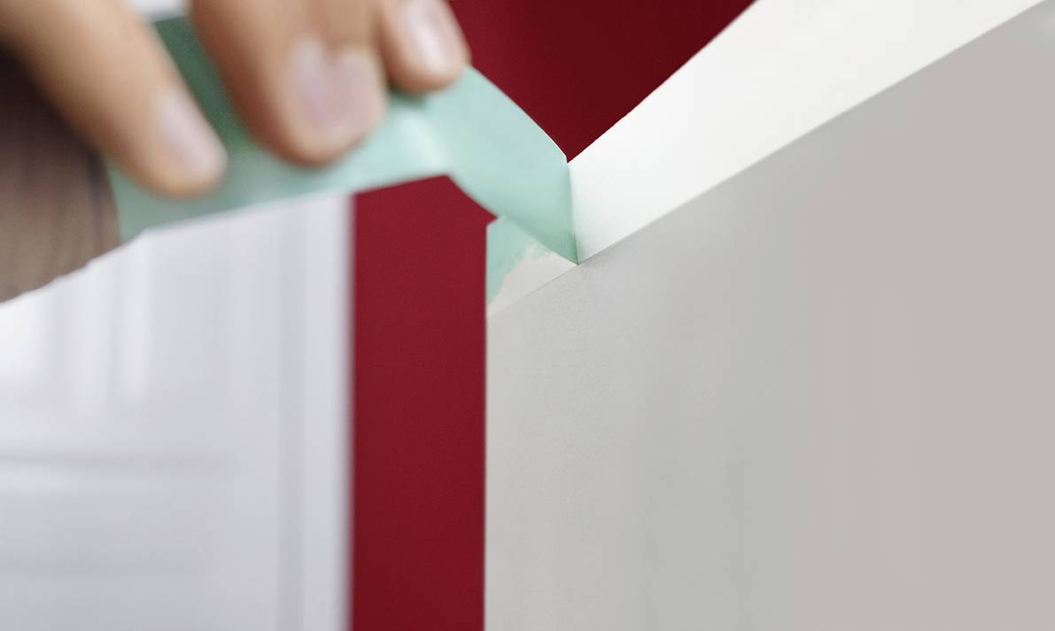 Hand entfernt Klebeband von einer frisch gestrichenen roten Wand.