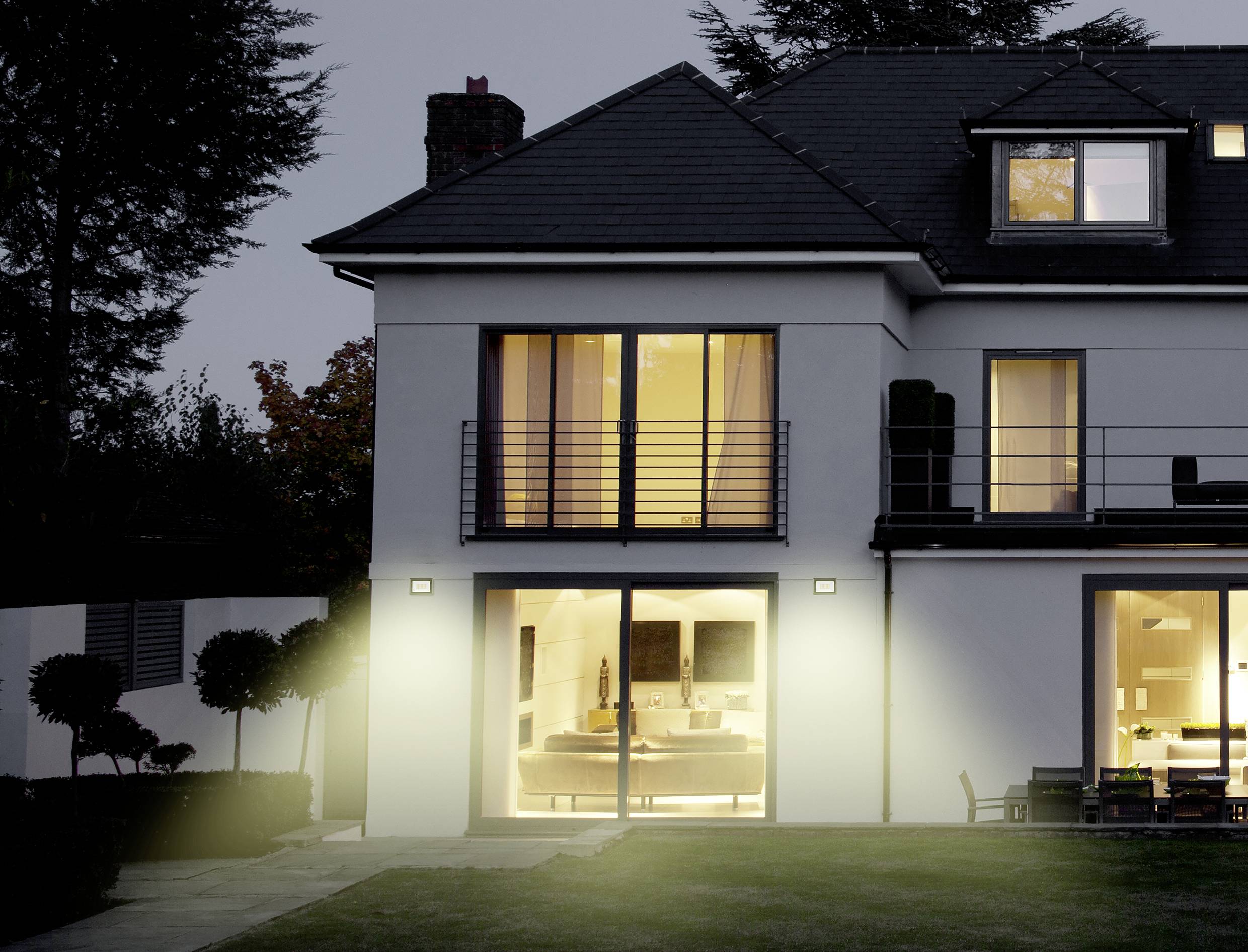 Zweistöckiges modernes Haus bei Abenddämmerung, mit beleuchtetem Innenraum und gepflegtem Garten.