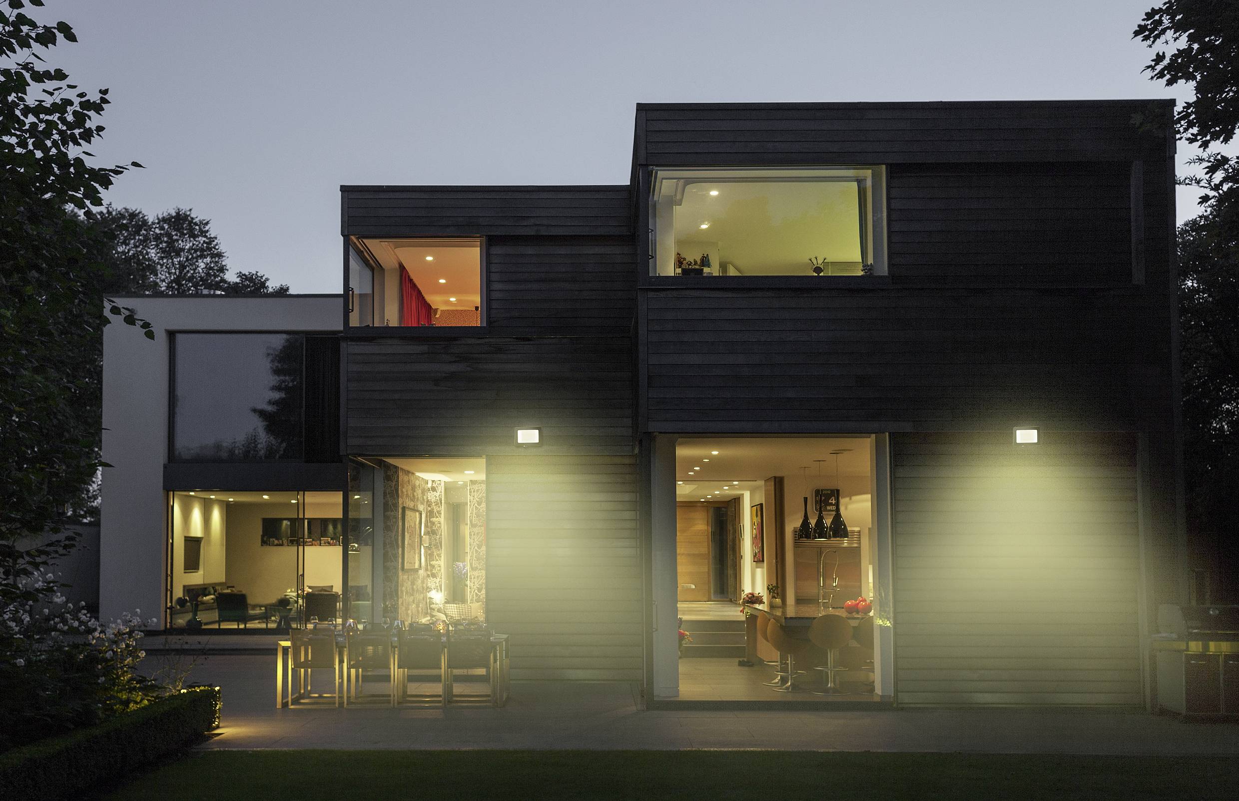 Ein modernes Haus bei Dämmerung, außen mit großen Fenstern. Licht leuchtet aus dem Inneren und beleuchtet den Garten sanft.