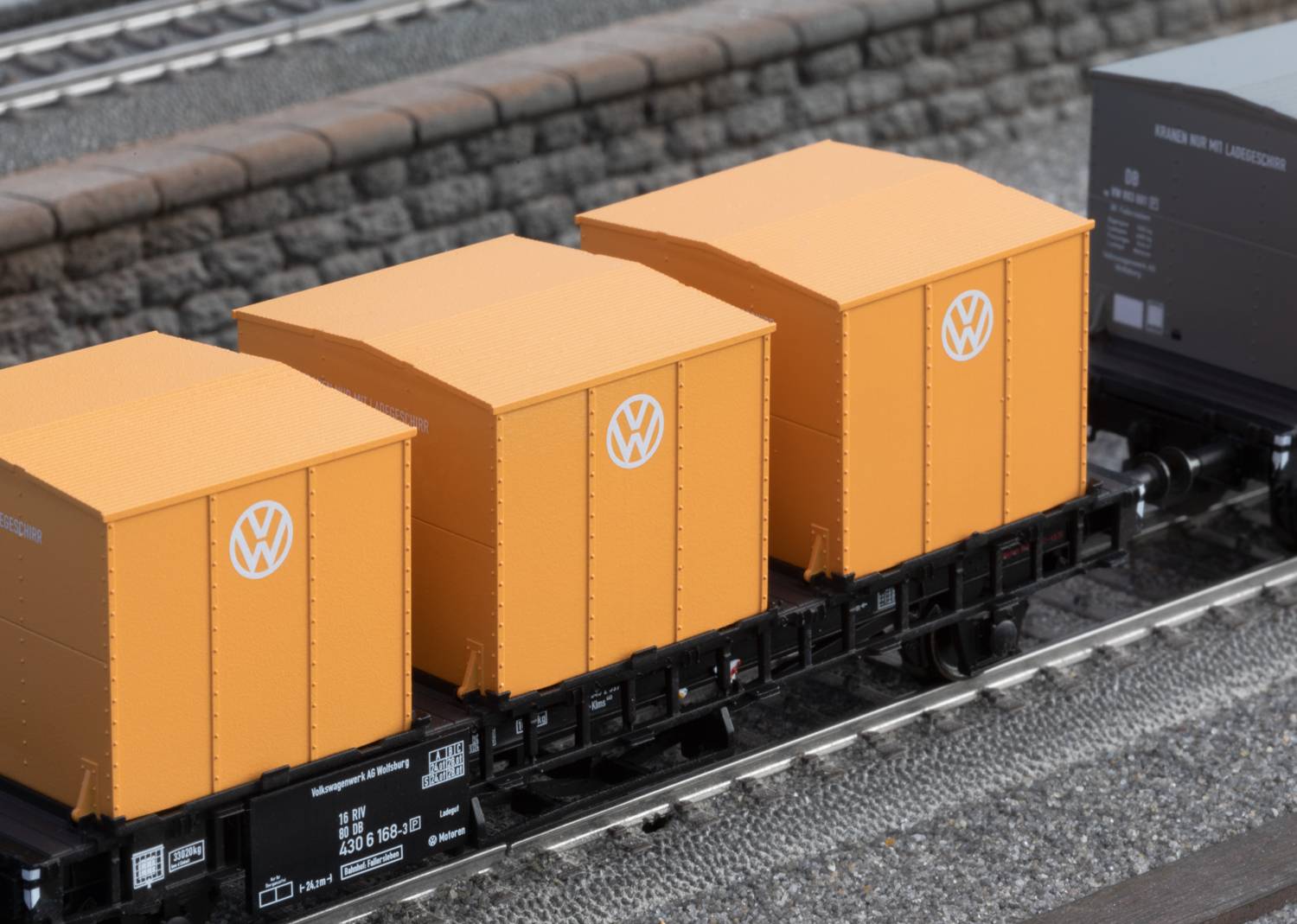 Drei gelbe Frachtcontainer mit Volkswagen-Logo auf einem Güterzug. Hintergrund zeigt Schienen und einen Steinwall.