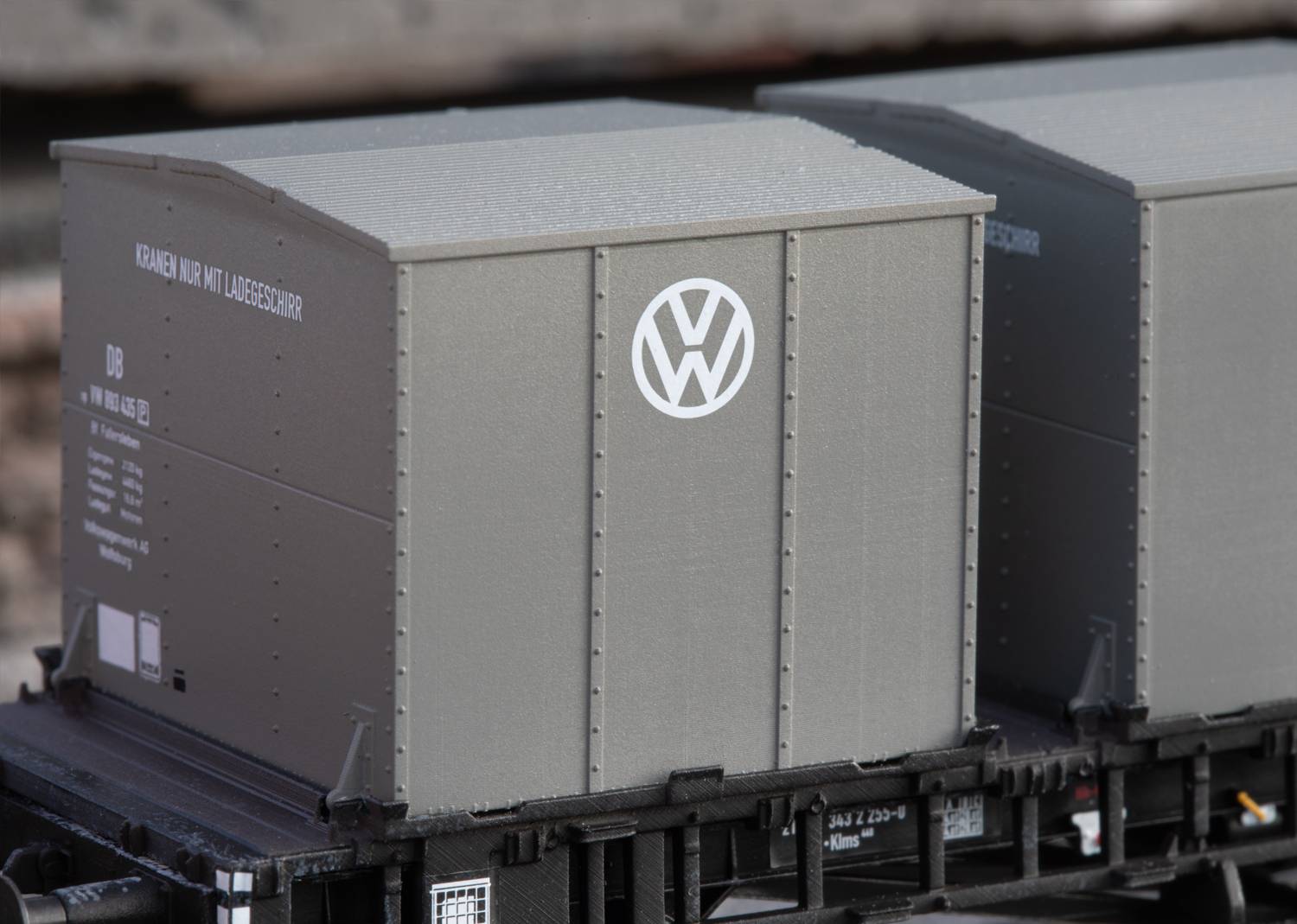 Grauer Güterwagen mit VW-Logo auf einem Eisenbahnwagen, wahrscheinlich für den Transport von Automobilkomponenten oder -teilen.