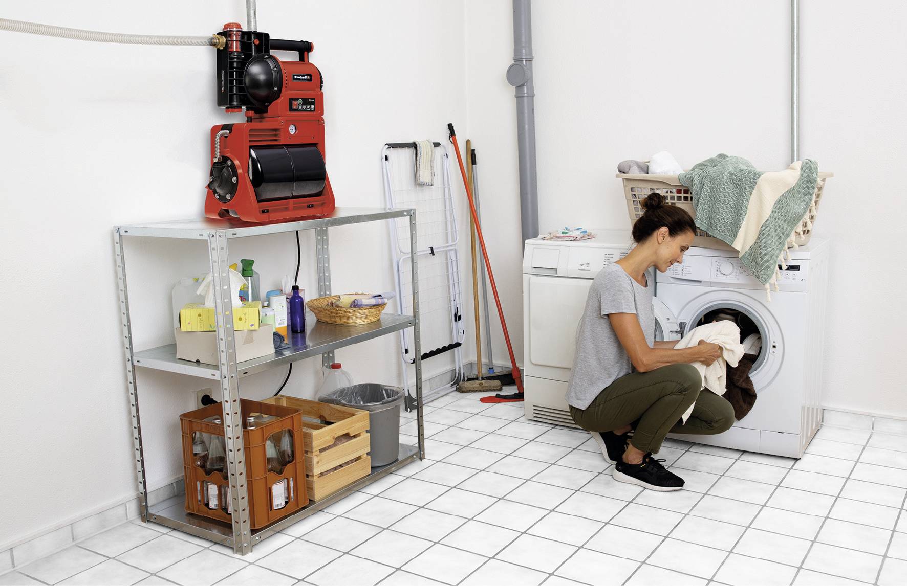 Eine Frau kniet vor einer Waschmaschine in einer hellen Waschküche. Sie belädt die Maschine mit Kleidungsstücken.