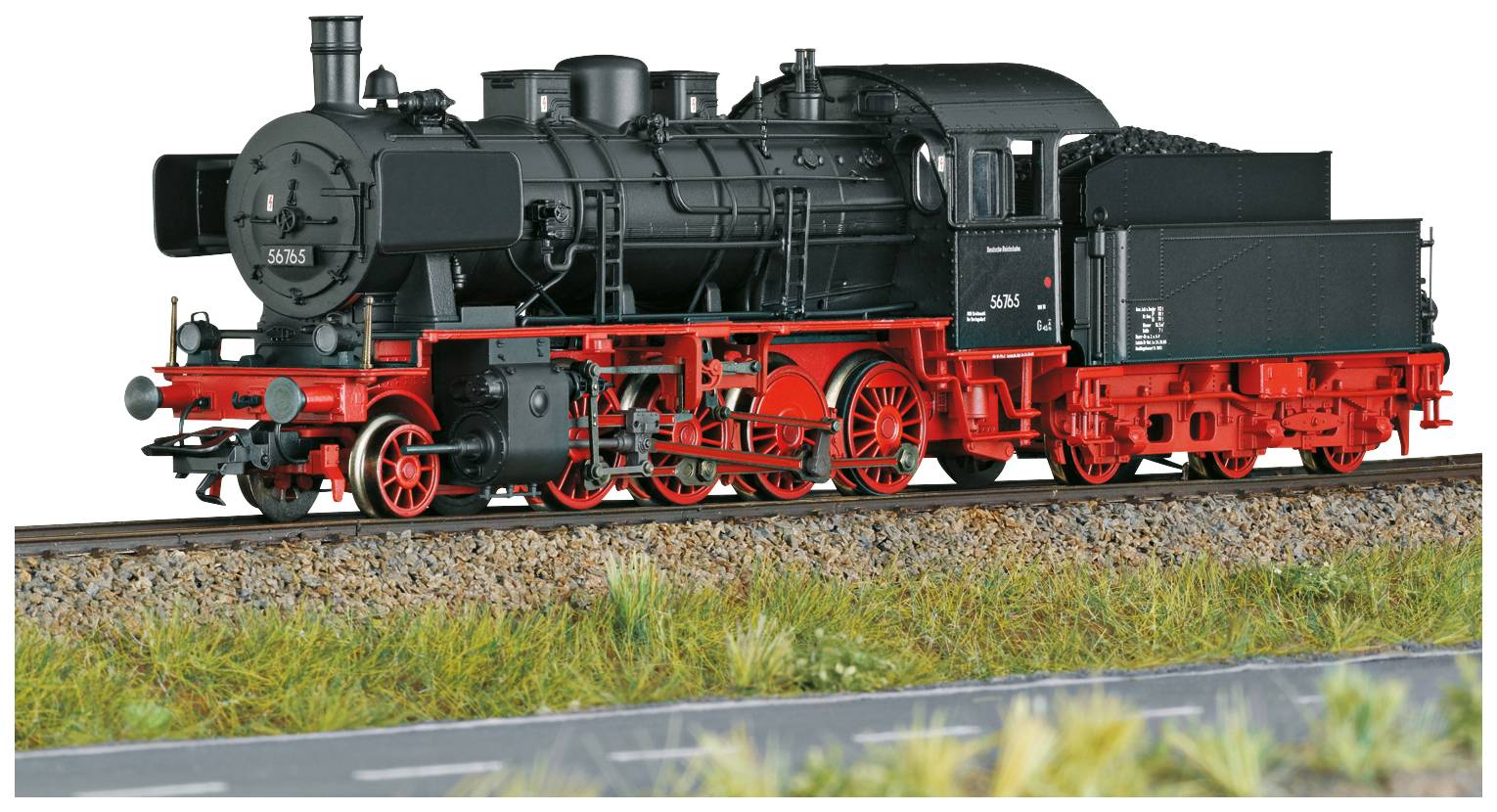 Schwarze Dampflokomotive mit rotem Fahrgestell auf einem Gleis, umgeben von Gras und einer Teerstraße im Vordergrund.