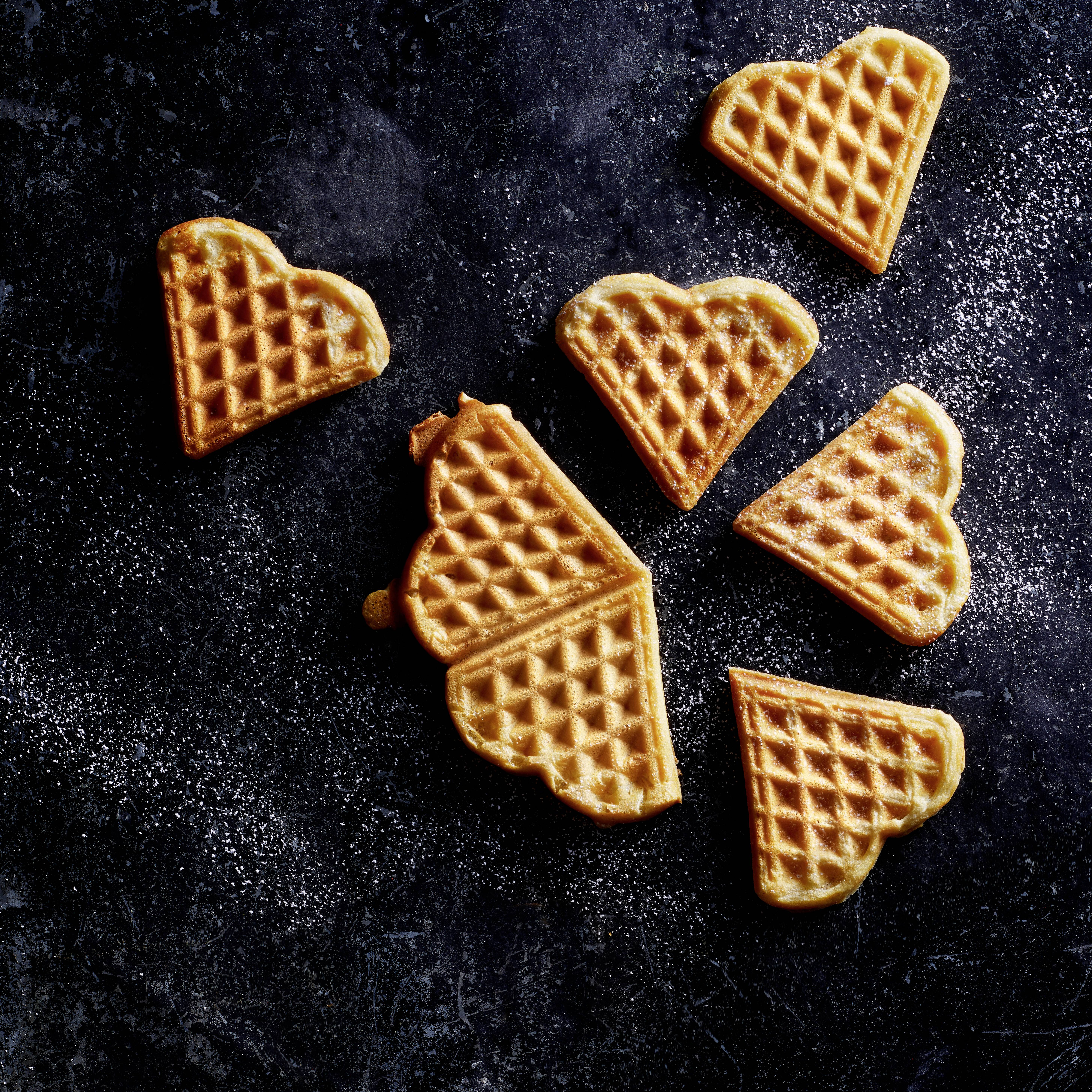 Herzförmige Waffeln auf dunklem Hintergrund, leicht mit Puderzucker bestreut. Perfekt für ein süßes, dekoratives Frühstücksbild.