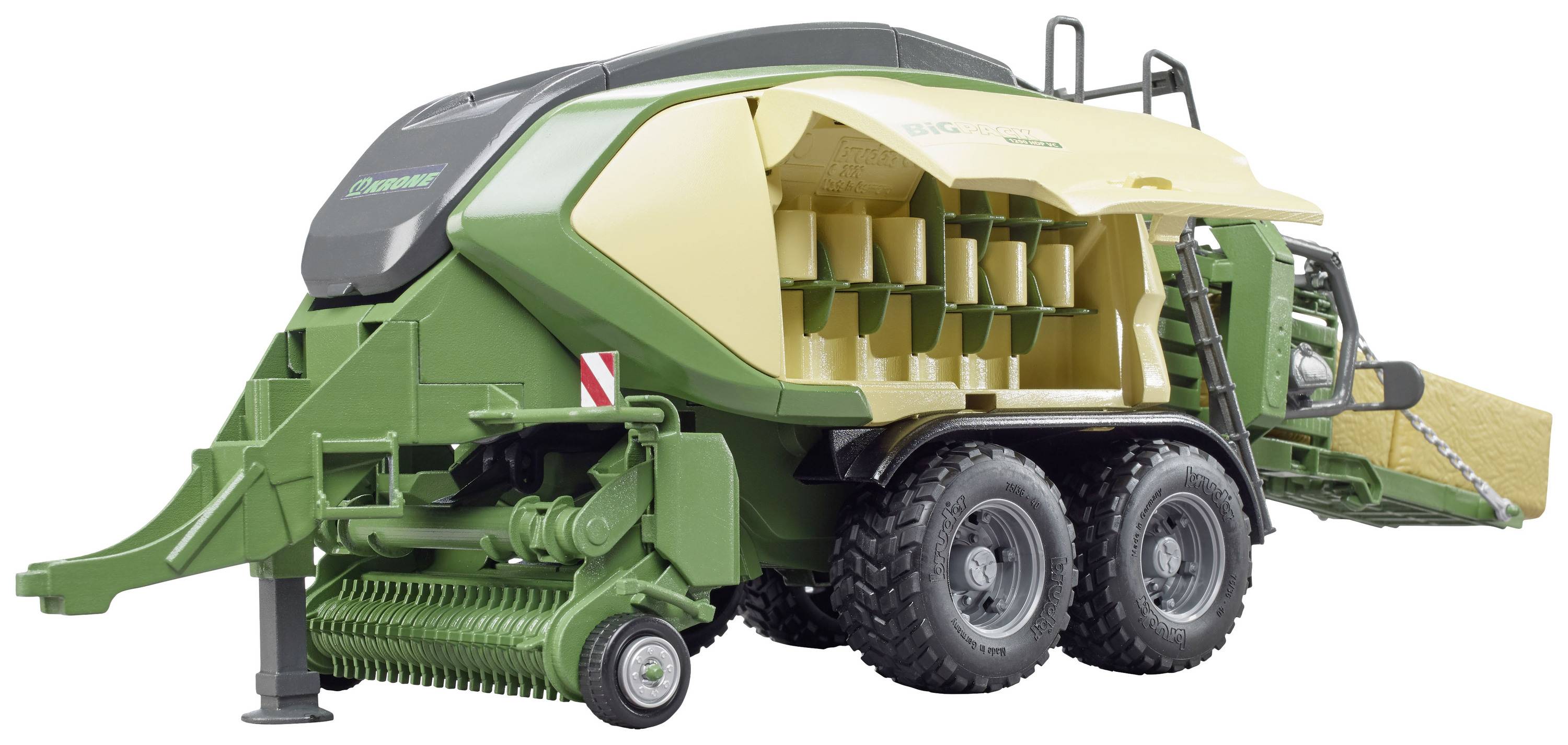 Grüner und gelber landwirtschaftlicher Ballenpressen-Anhänger auf Rädern, mit geöffneter Seitenklappe, die Innenmechanik zeigt.