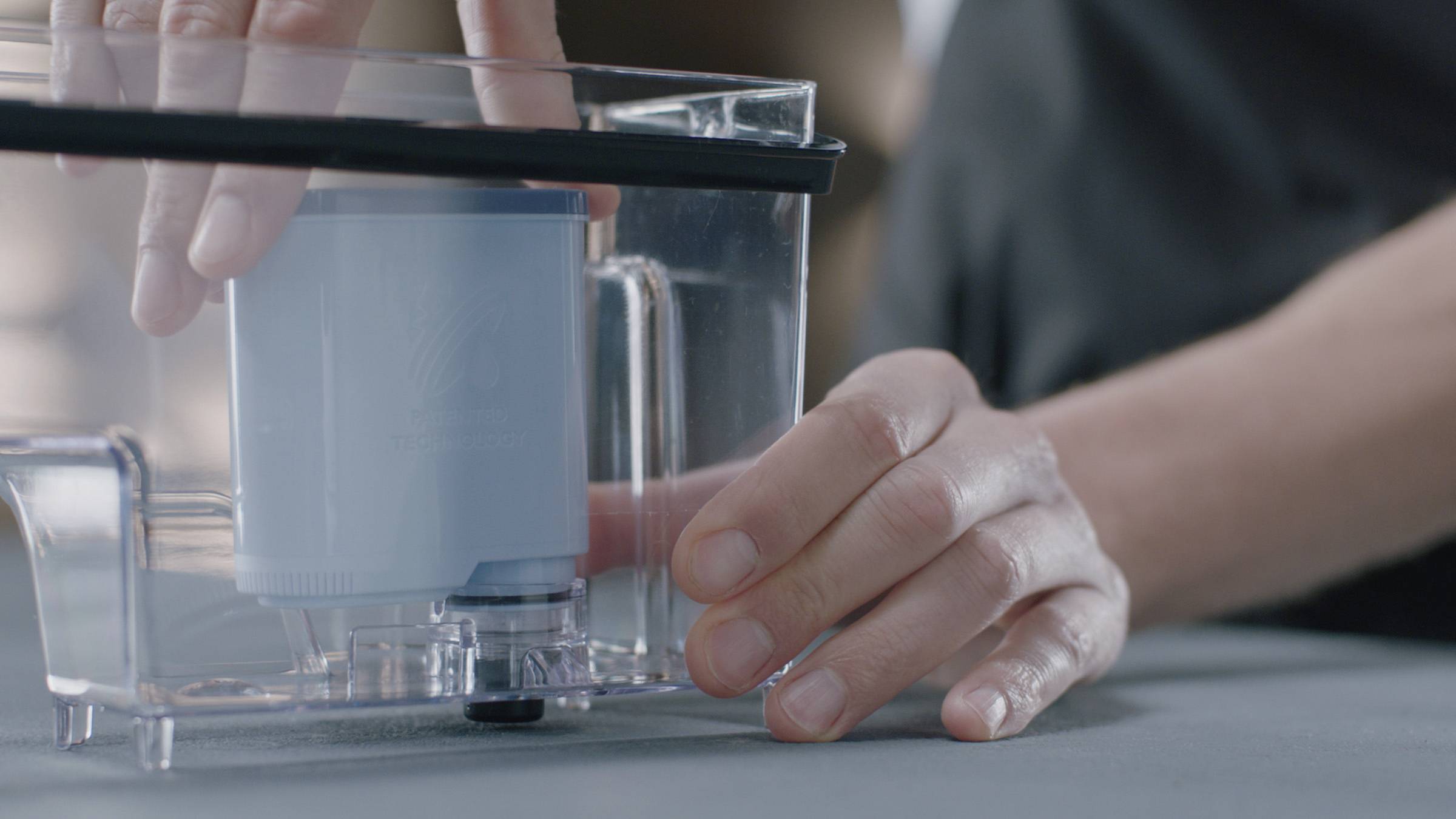 Person installiert einen blauen Wasserfilter in einen transparenten Behälter. Hände sind im Fokus, zeigen sorgfältige Bedienung.
