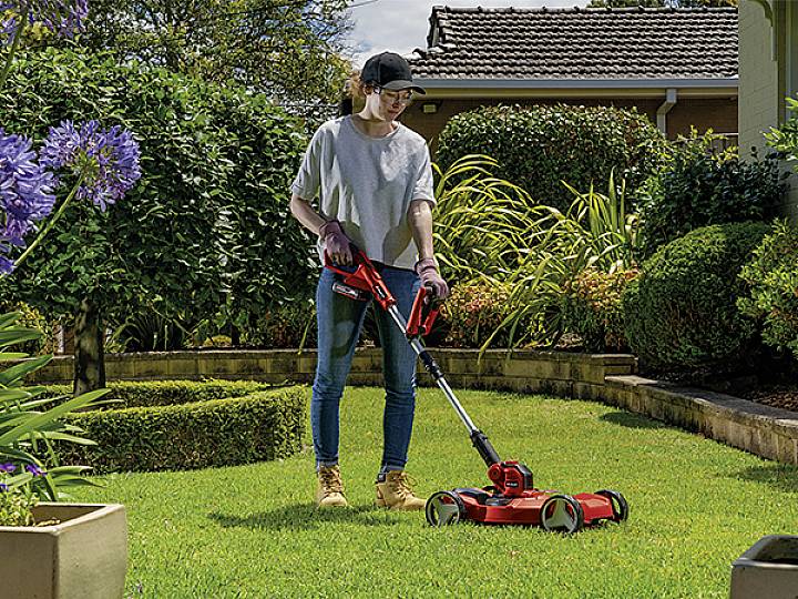 Eine Person mäht einen Rasen mit einem elektrischen Rasenmäher in einem gepflegten Garten.