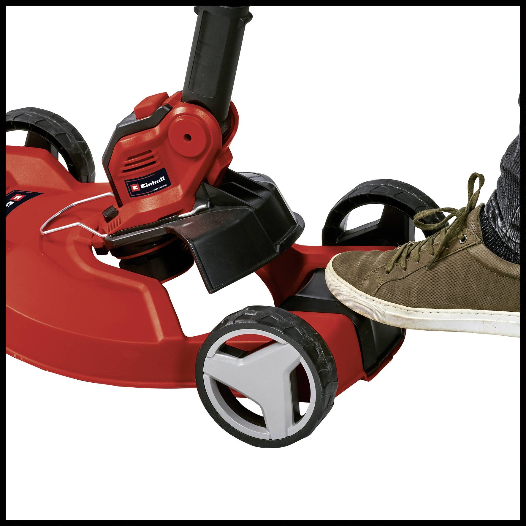 Ein roter Rasenmäher mit einem schwarzen Griff, im Einsatz gezeigt. Ein Fuß in einem braunen Schuh drückt auf das Gerät.
