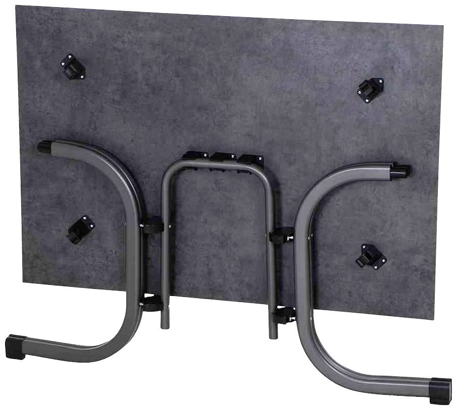 Ein umgeklappter, rechteckiger Tisch mit Metallbeinen und einer dunklen Tischplatte, zeigt den Mechanismus zur Beinbefestigung.