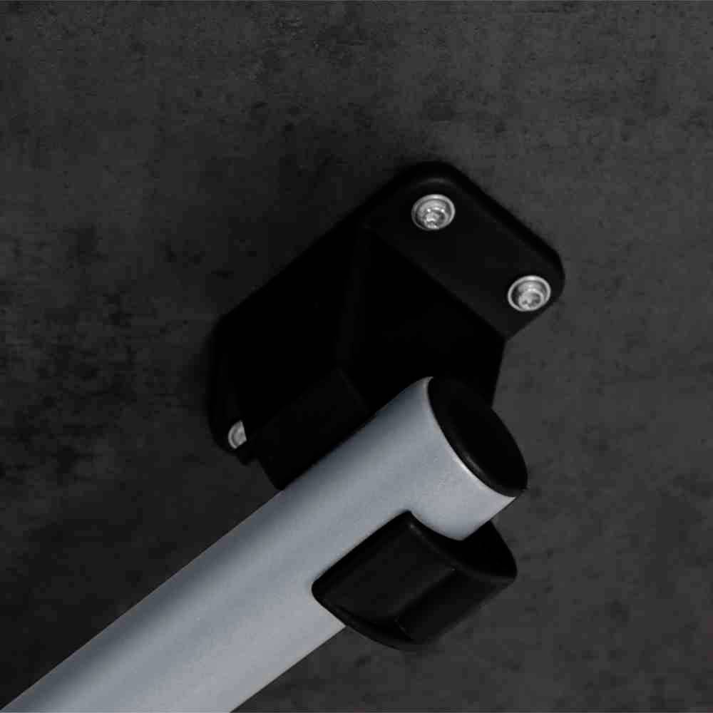 Wandhalterung mit montiertem silbernem Rohr an einer grauen Betonwand, befestigt mit schwarzen Schrauben. Geeignet für industrielle Zwecke.