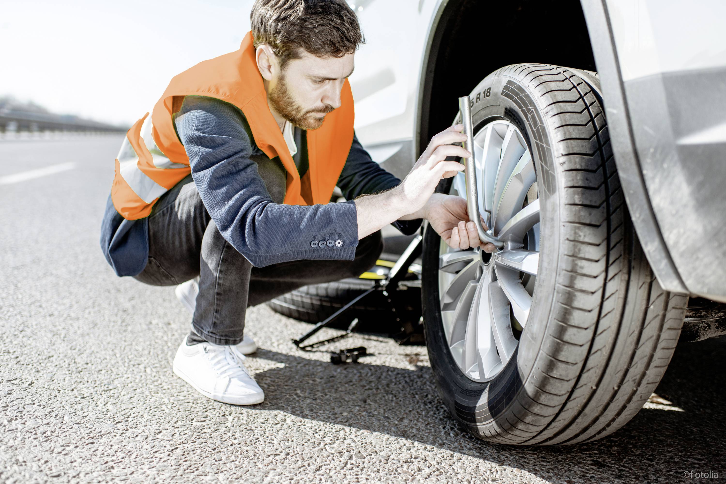 Ein Mann in Sicherheitsweste wechselt den Reifen eines Autos am Straßenrand.