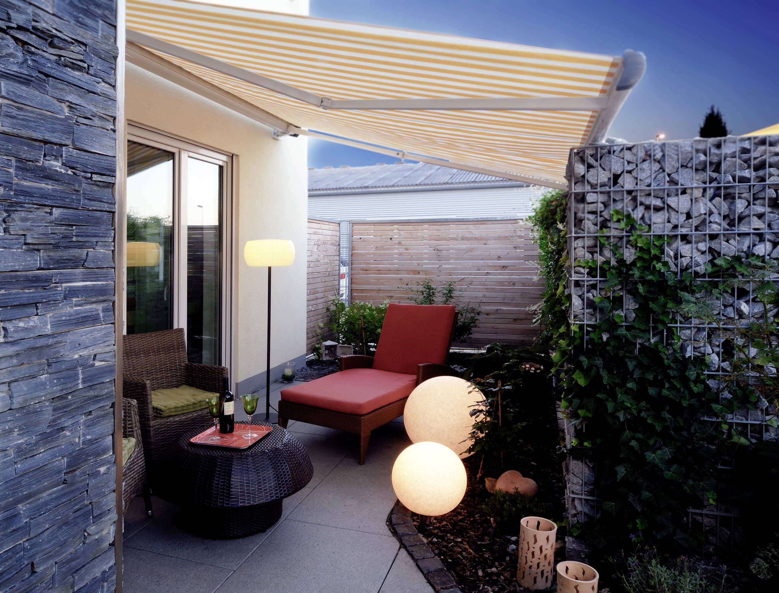 Überdachte Terrasse mit gemütlichen Möbeln, Beleuchtungskugeln und Pflanzen in einem modernen Garten.