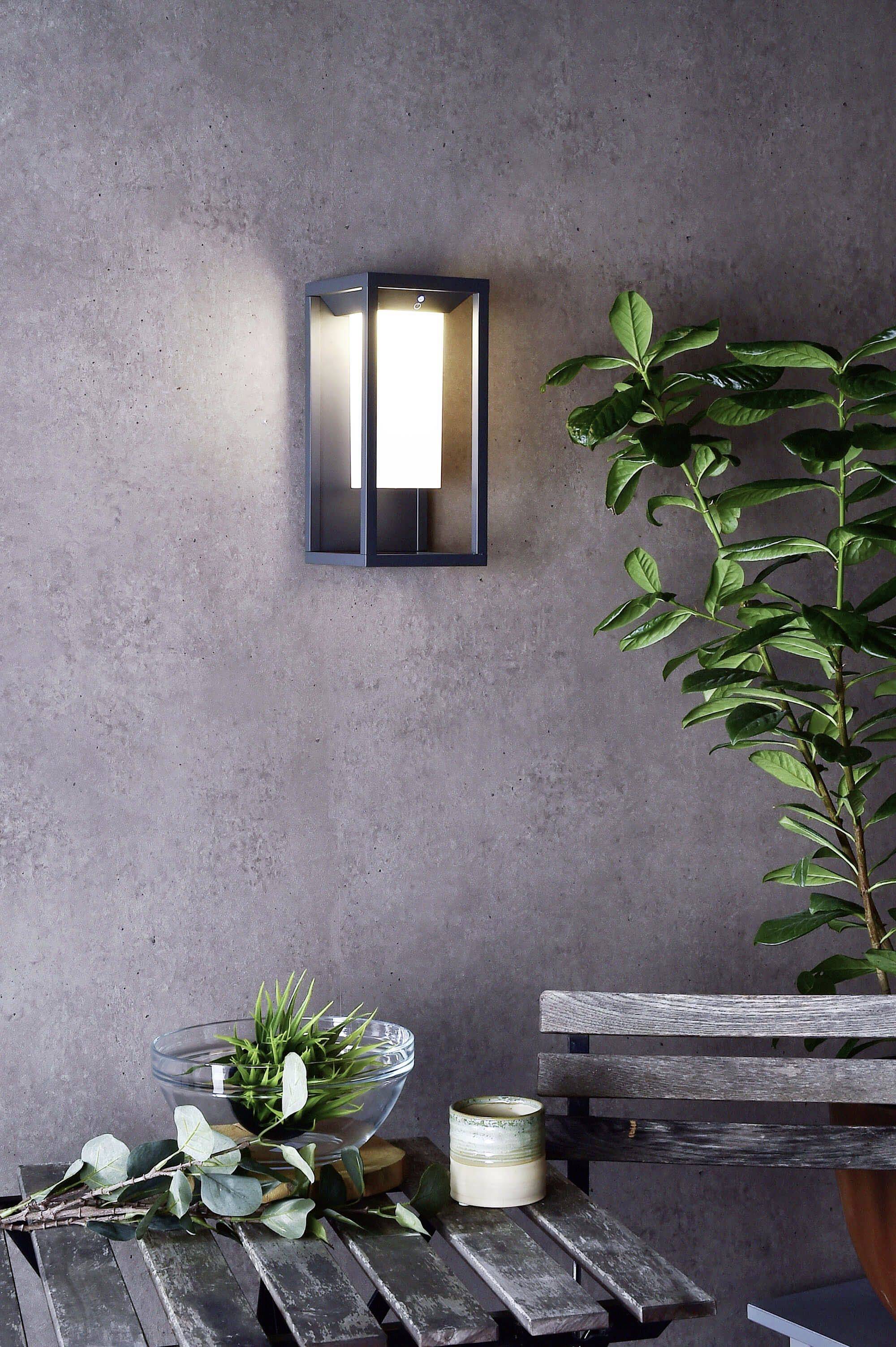 Wandleuchte leuchtet sanft neben einem Tisch mit einer Pflanze und Kerze in einem modernen, minimalistischen Raum.