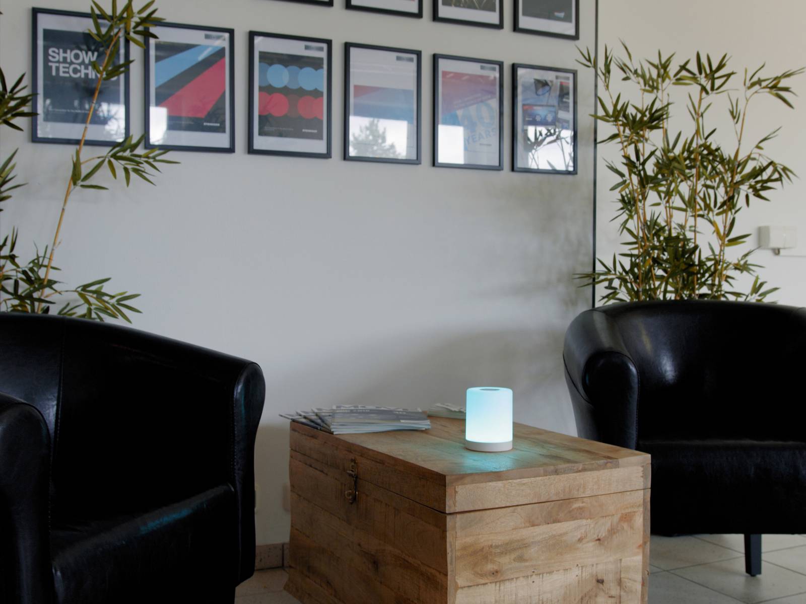 Zwei schwarze Sessel umgeben einen Holztisch mit einem leuchtenden, blauen Licht. An der Wand hängen gerahmte Bilder.