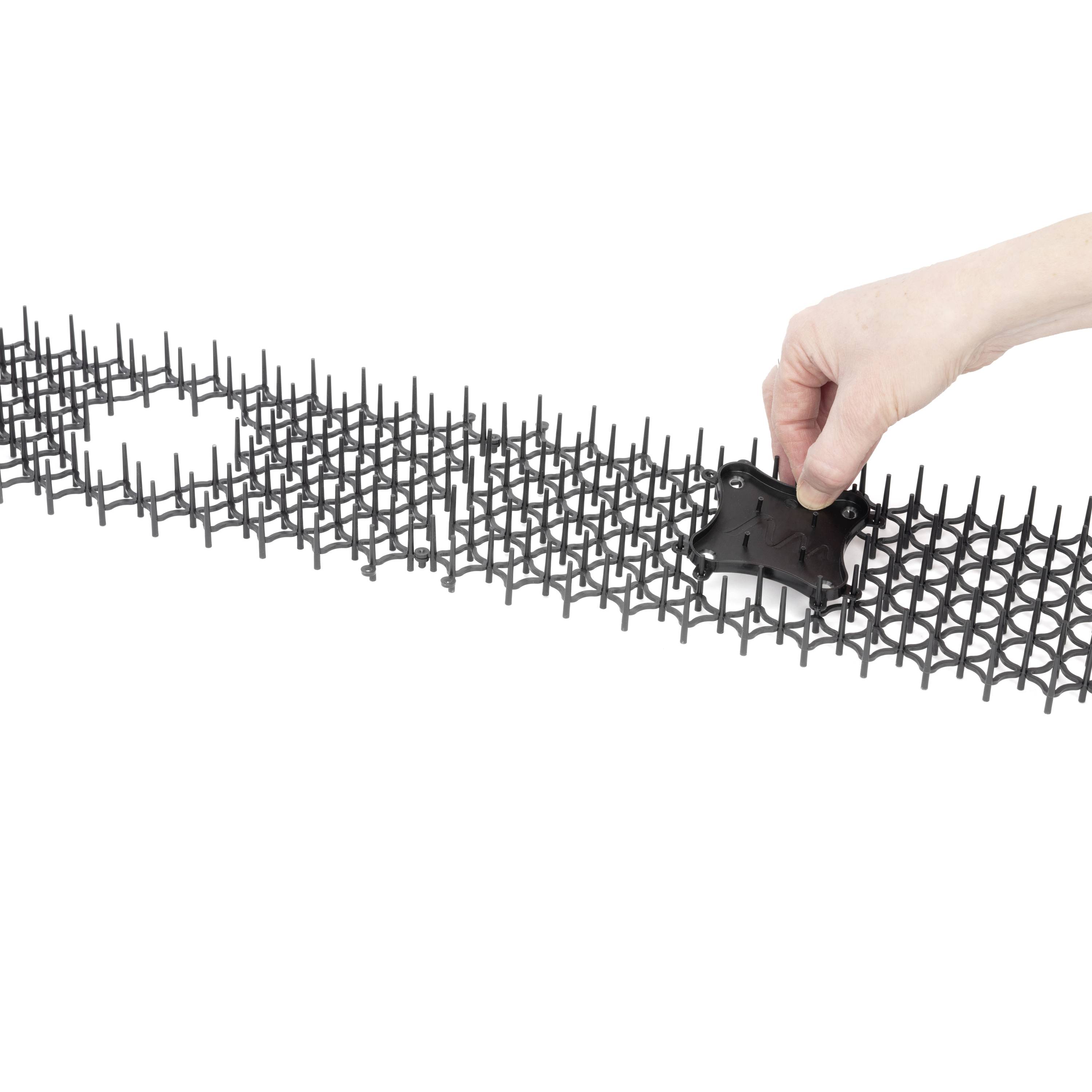 Eine Hand fügt ein einzelnes schwarzes Bauteil in eine Gitterstruktur ein. Die Struktur scheint modular und erweiterbar zu sein.