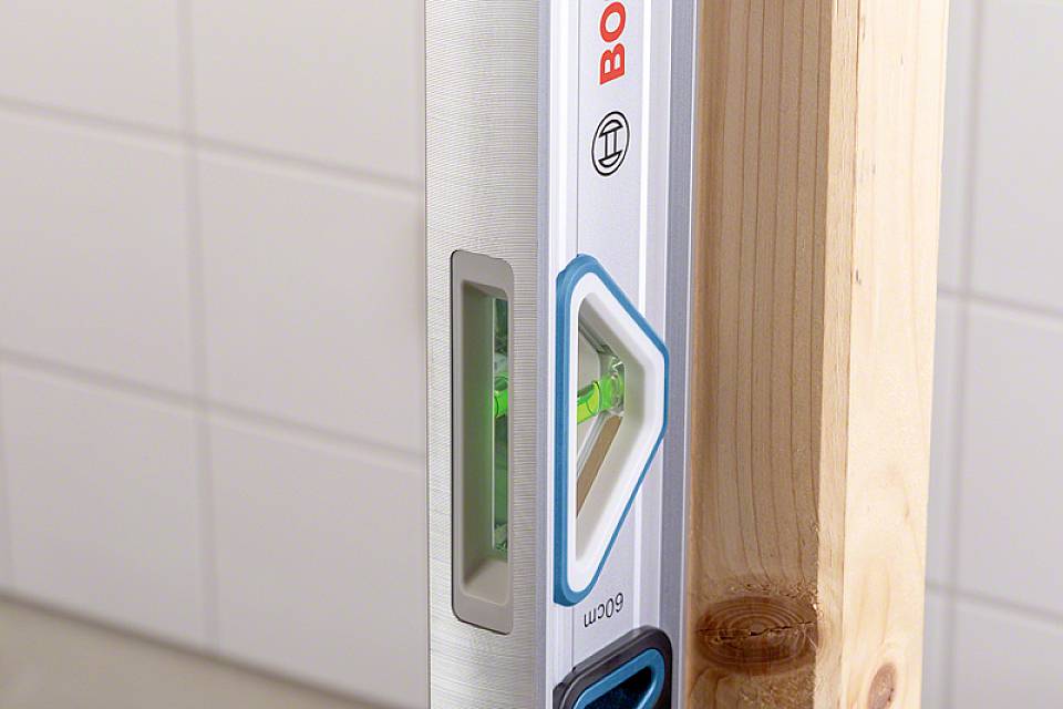 Wasserwaage mit einer Holzlatte auf einer gefliesten Oberfläche, zeigt eine genaue Ausrichtung an.