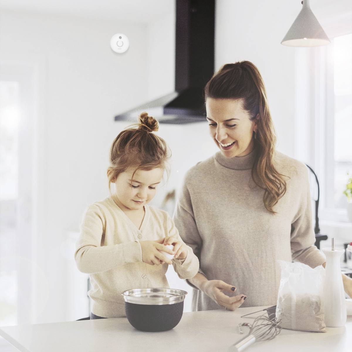 Frau und Kind backen gemeinsam in einer hellen Küche. Beide lächeln und das Kind befüllt eine Schüssel mit Zutaten.