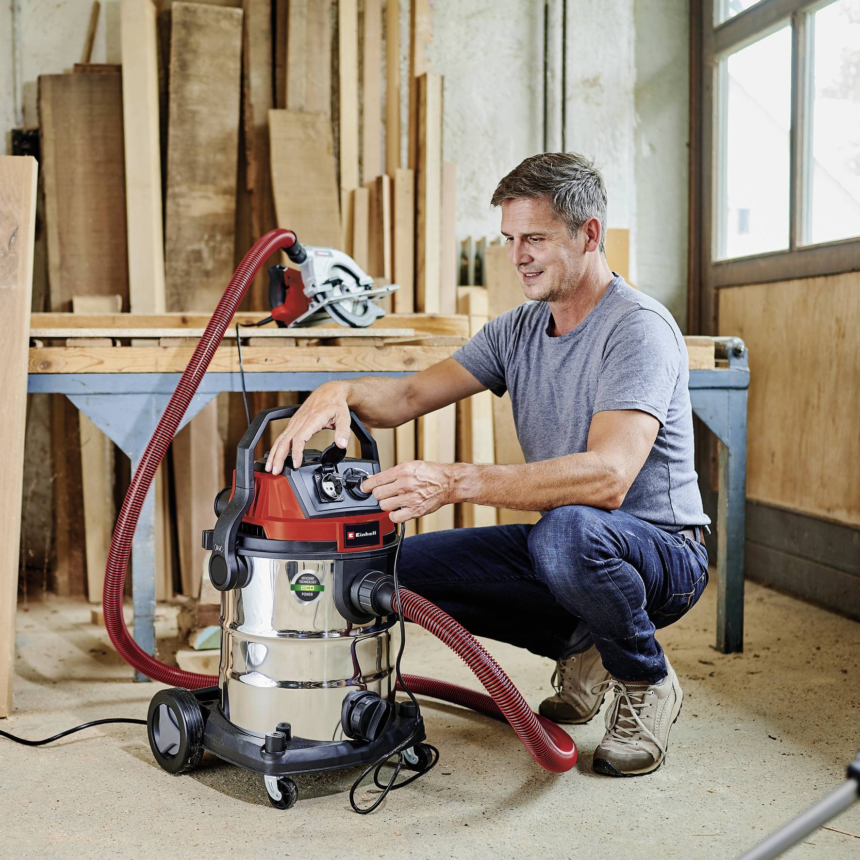 Mann in Werkstatt benutzt Nass-Trockensauger neben Werkbank; im Hintergrund liegt eine Säge.
