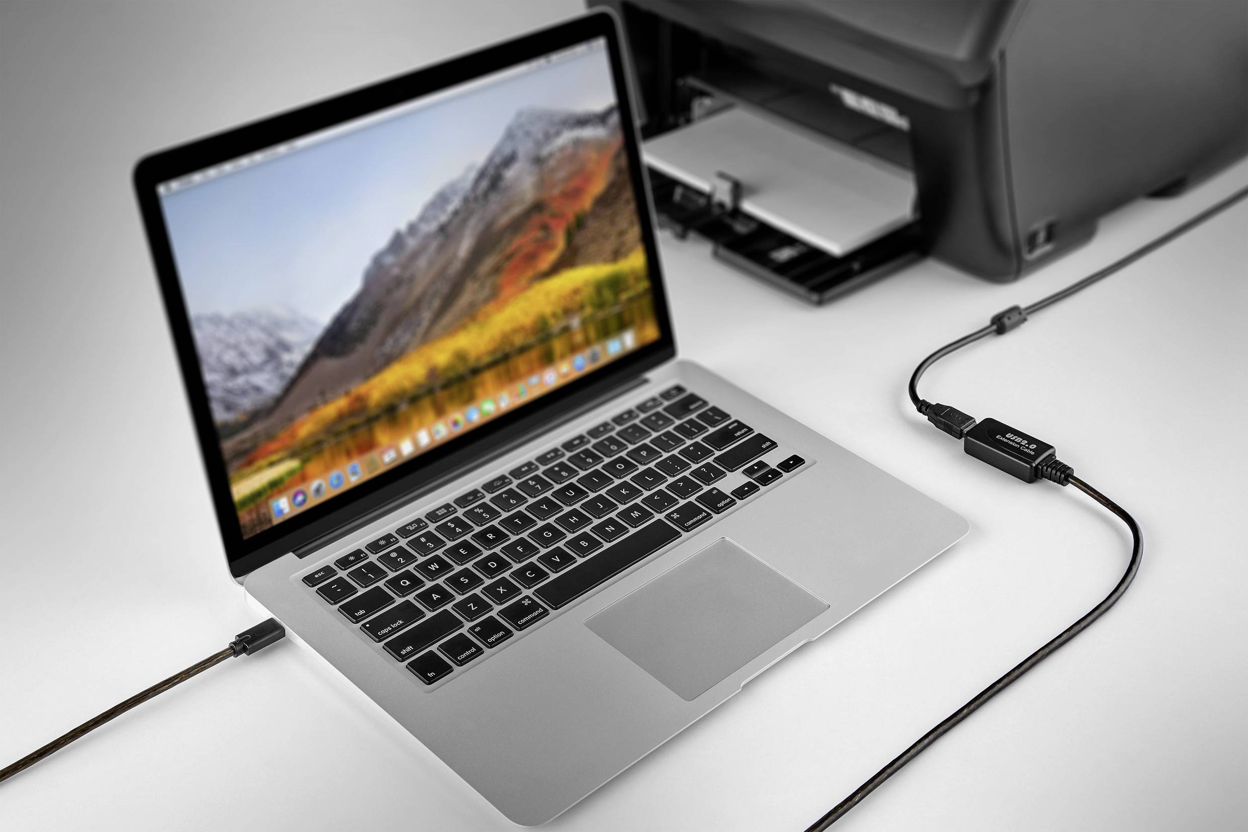 Ein Laptop ist über ein Kabel mit einem Drucker verbunden. Der Laptop zeigt eine Berglandschaft auf dem Bildschirm.