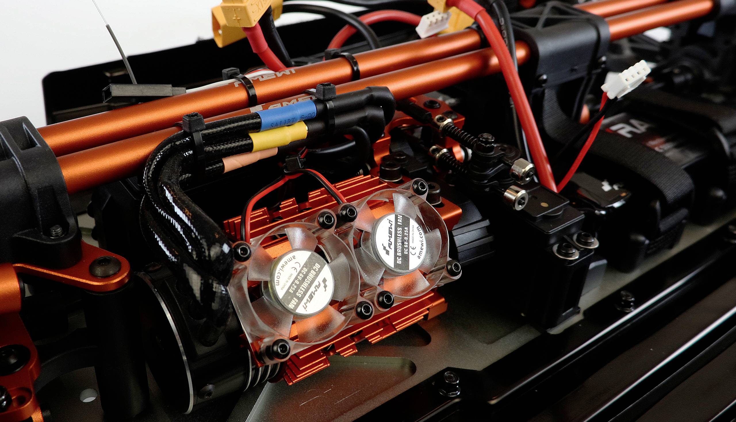 Nahaufnahme eines RC-Autoteils mit mehreren Kabeln und Lüftern. Die Struktur ist metallisch mit schwarzen und roten Komponenten.