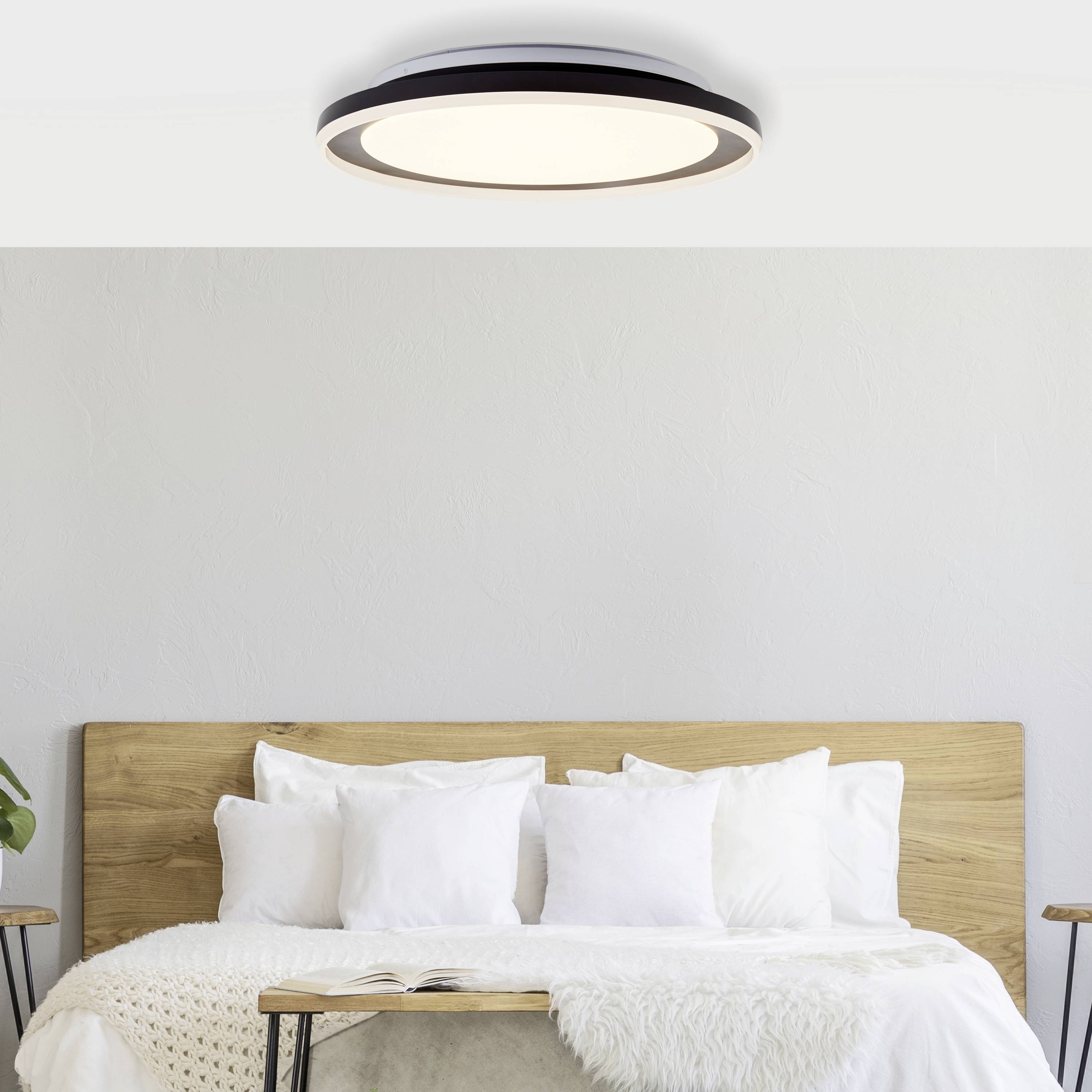 Ein modernes Schlafzimmer mit einem Holzbett, weißen Kissen, einer Decke und einer runden Deckenleuchte über dem Bett.