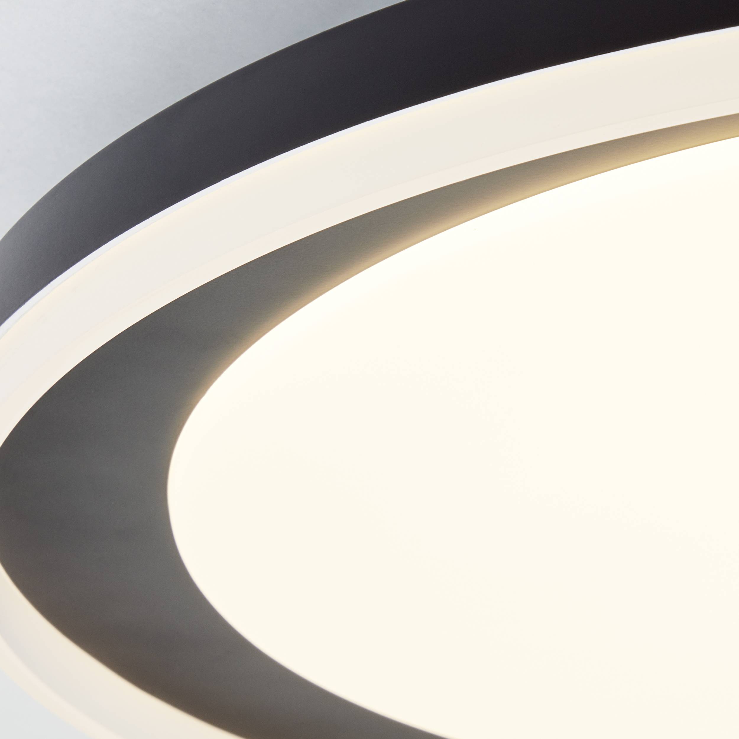 Eine runde, moderne Deckenleuchte leuchtet in weißem Licht, umgeben von einem schwarzen Rand, gegen einen grauen Hintergrund.