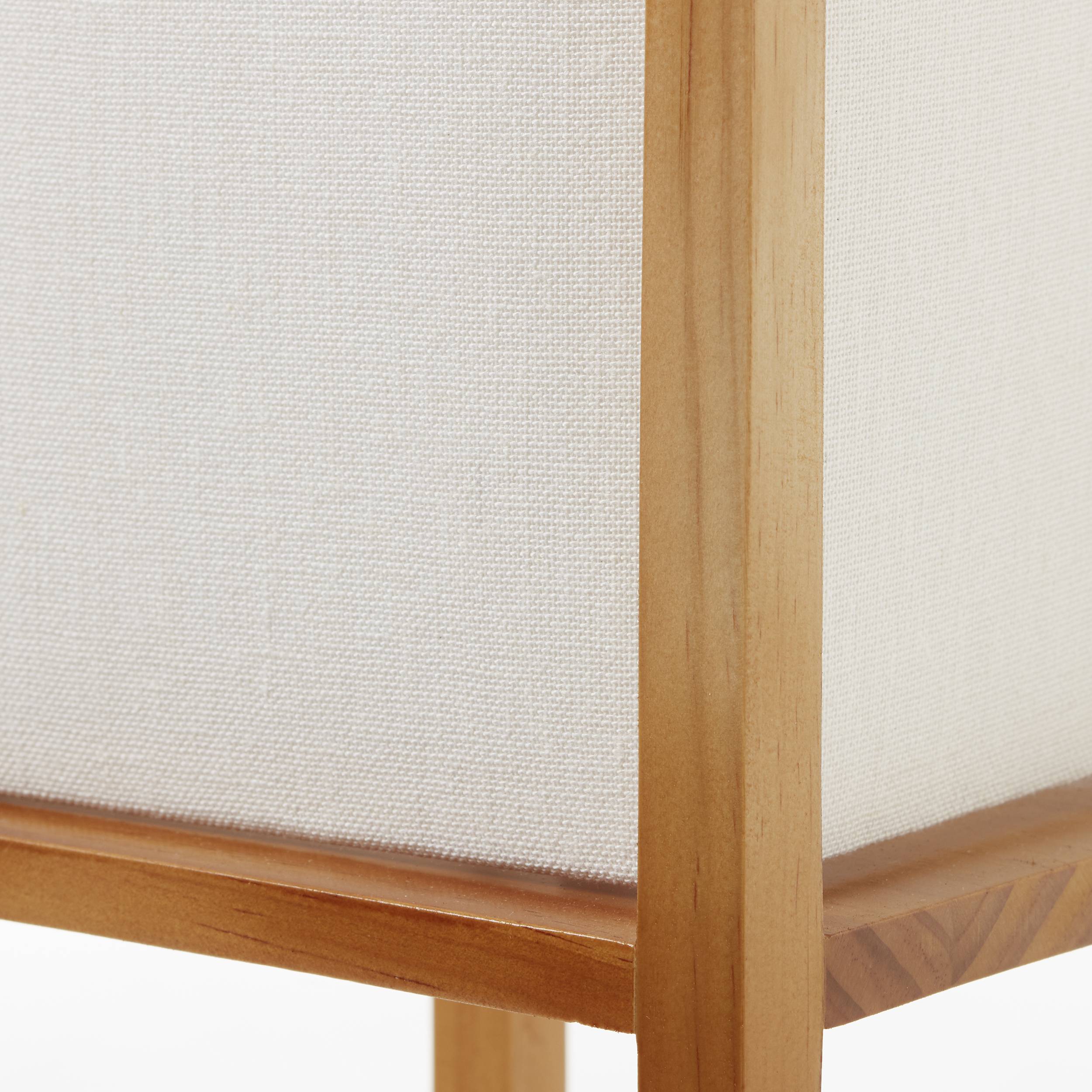 Ausschnitt einer Tischlampe mit rechteckigem Sockel aus Holz und einem weißen Stoffschirm. Schlichtes, modernes Design.