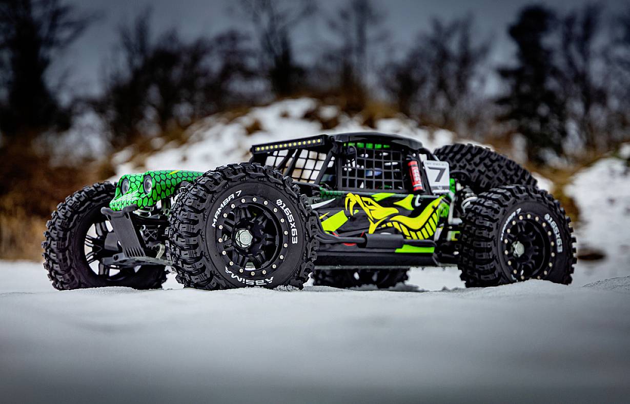 Ein ferngesteuertes Auto mit aggressivem Design und grüner Zeichnung auf der Karosserie fährt über eine schneebedeckte Fläche.