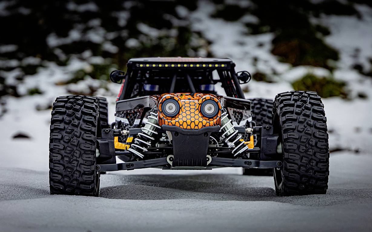 Ein ferngesteuertes Auto mit großen Geländereifen, das frontal im Schnee steht. Das Design der Karosserie erinnert an ein Gesicht.