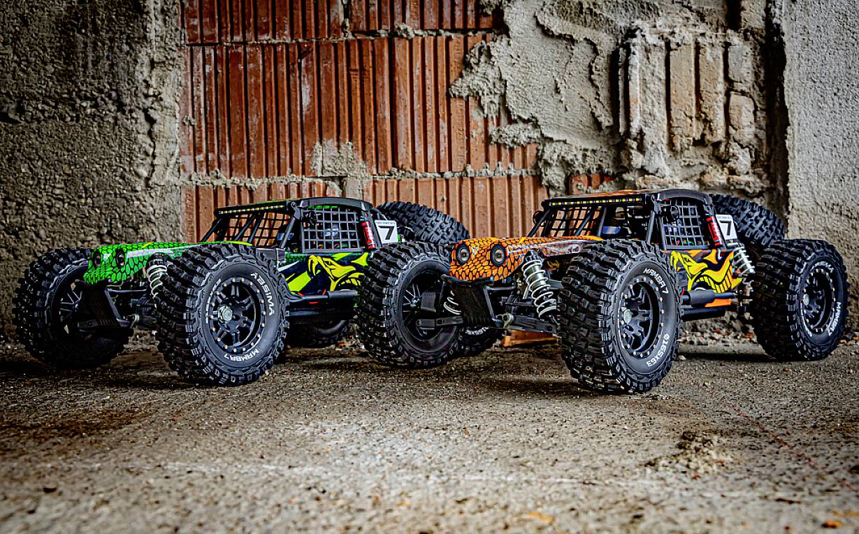 Drei farbenfrohe ferngesteuerte Geländewagen sind nebeneinander auf einem Betonboden vor einer rauen Ziegelmauer platziert.
