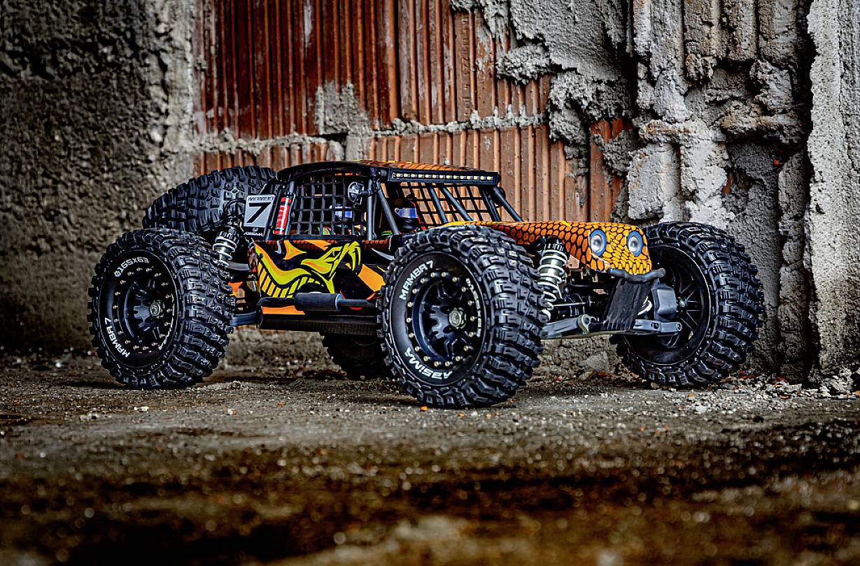 Ein ferngesteuertes Auto mit großen Reifen und buntem Design steht vor einer Wand aus rohem Beton und Ziegeln.