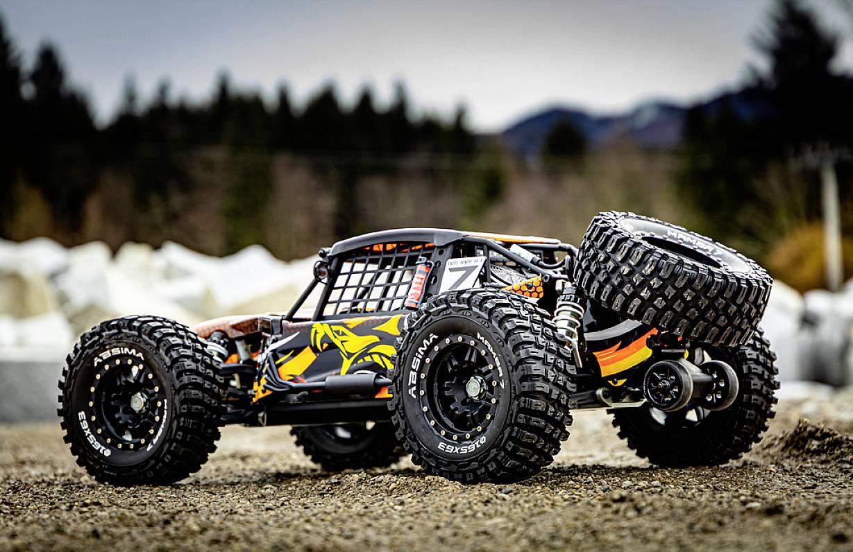 Ein ferngesteuertes, geländegängiges Modellauto mit robusten Reifen steht auf einem unbefestigten Weg, umgeben von verschwommenem Waldhintergrund.