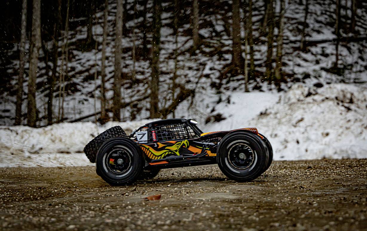 Ein ferngesteuertes Auto in Bewegung auf einem verschneiten Waldweg. Das Auto hat ein auffälliges, buntes Design.