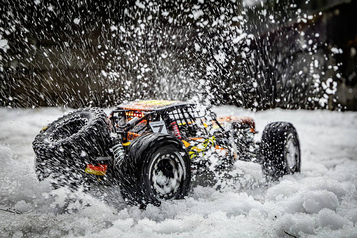 Ein ferngesteuertes Auto spritzt Schnee auf. Es fährt dynamisch, umgeben von Schneeflocken, was seine Geschwindigkeit und Beweglichkeit verdeutlicht.