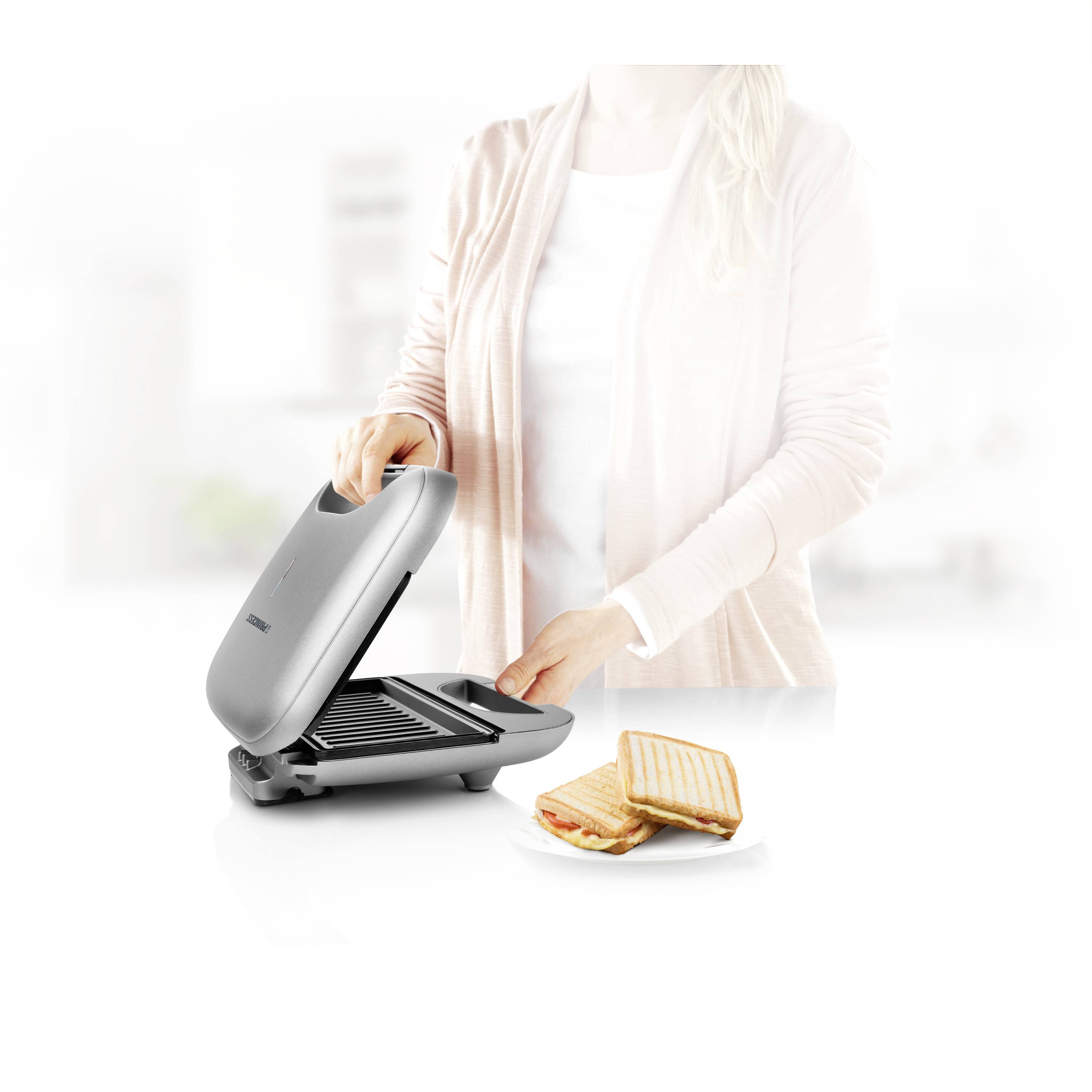 Eine Person benutzt einen Sandwichmaker. Daneben liegt ein Teller mit fertigen Toastsandwiches.