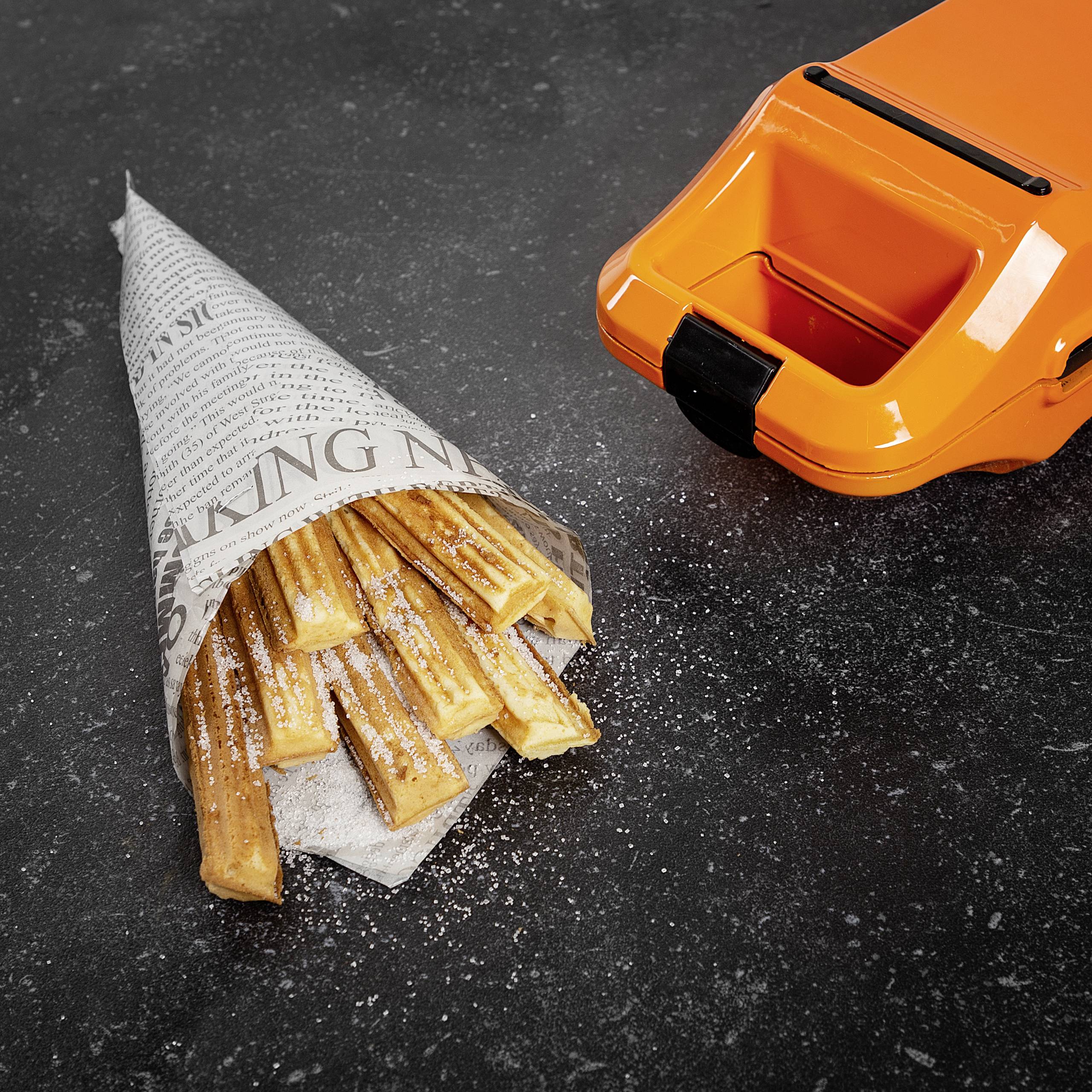 Waffelstäbchen in Papierkegel auf dunklem Hintergrund neben hellorangefarbenem Waffeleisen. Mit Puderzucker bestreut.