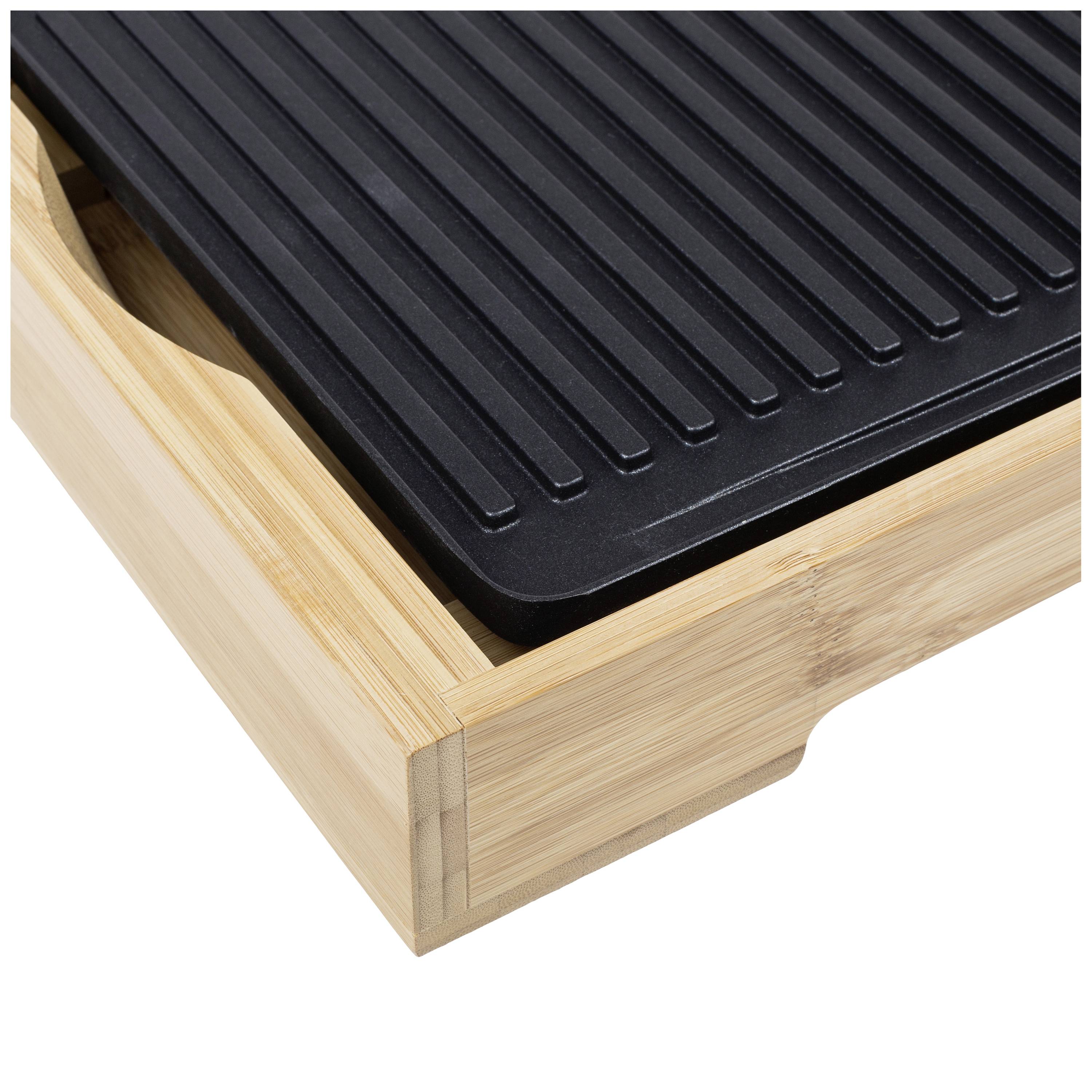 Schwarze Grillplatte auf hölzernem Tablett. Die Platte hat Rillen und liegt auf der rechten Seite des rechteckigen Holztabletts.