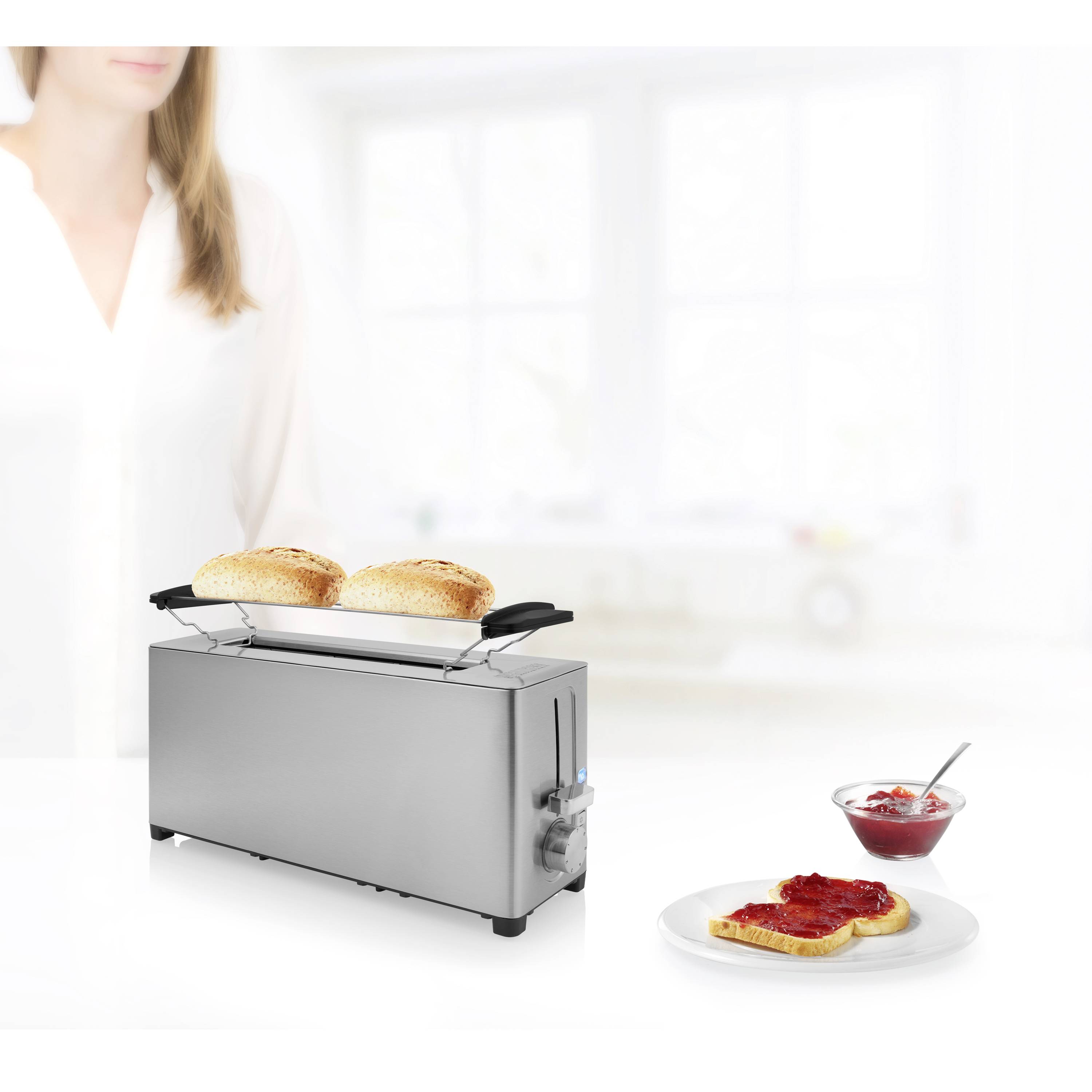 Ein silberner Toaster mit zwei goldbraunen Toastscheiben. Daneben auf einem Teller liegt geröstetes Brot mit roter Marmelade. Im Hintergrund eine Person.