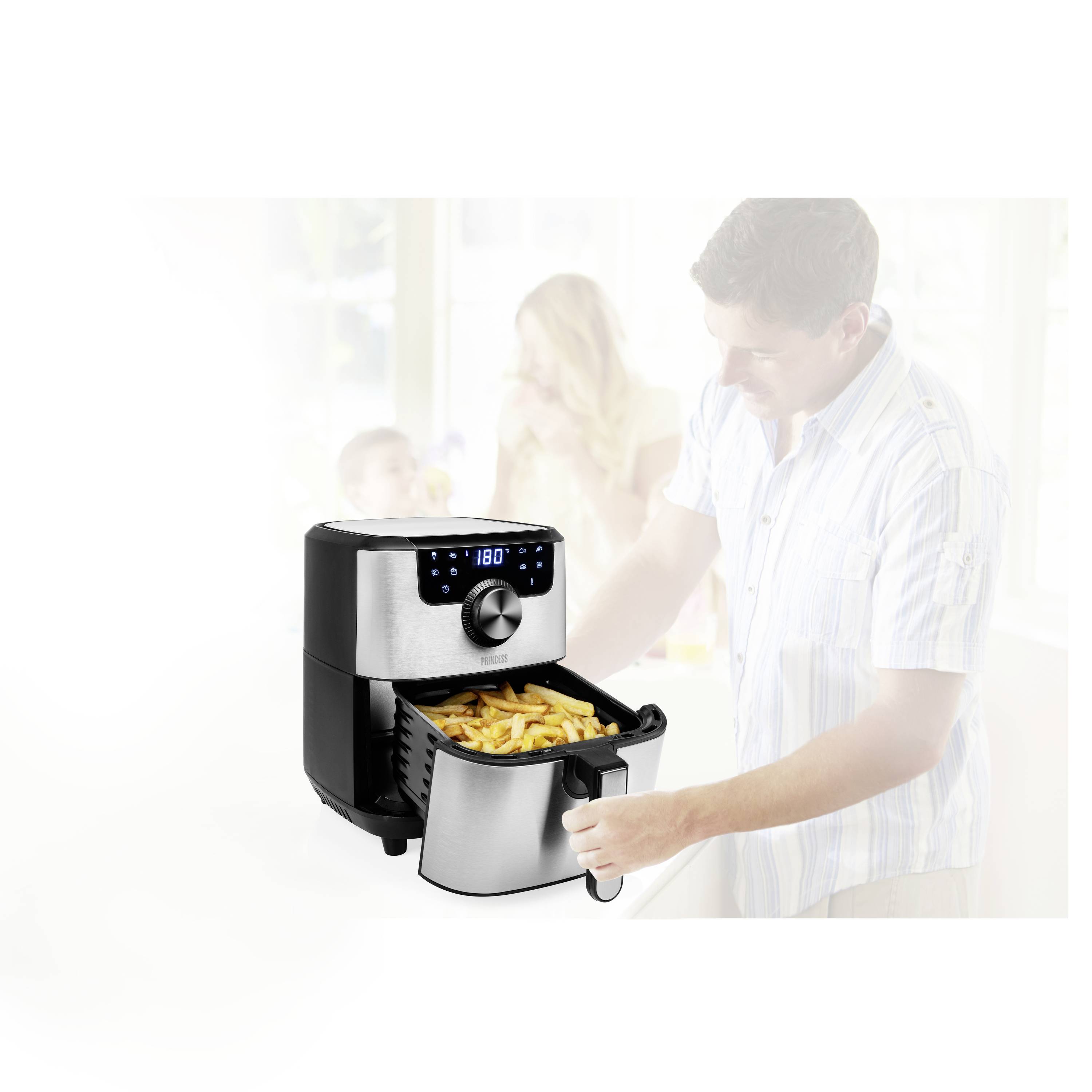Eine Heißluftfritteuse mit digitalem Display brät Pommes Frites. Im Hintergrund sind unscharf eine Familie mit zwei Kindern zu sehen.