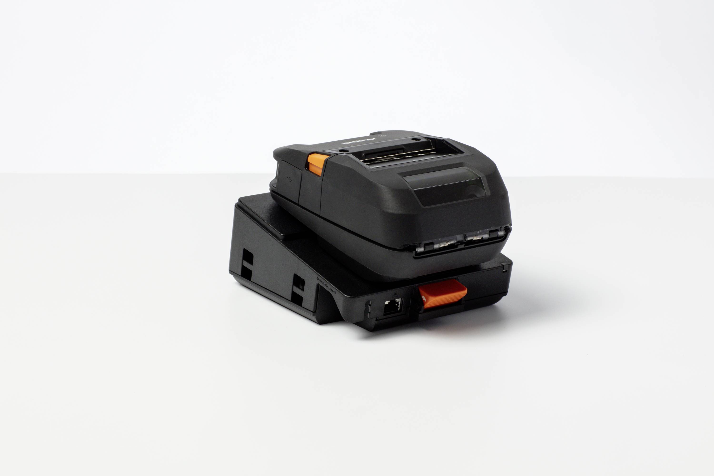 Ein tragbarer, schwarzer Etikettendrucker mit orangefarbenem Knopf, auf einer Ladestation. Ideal für mobiles Drucken.