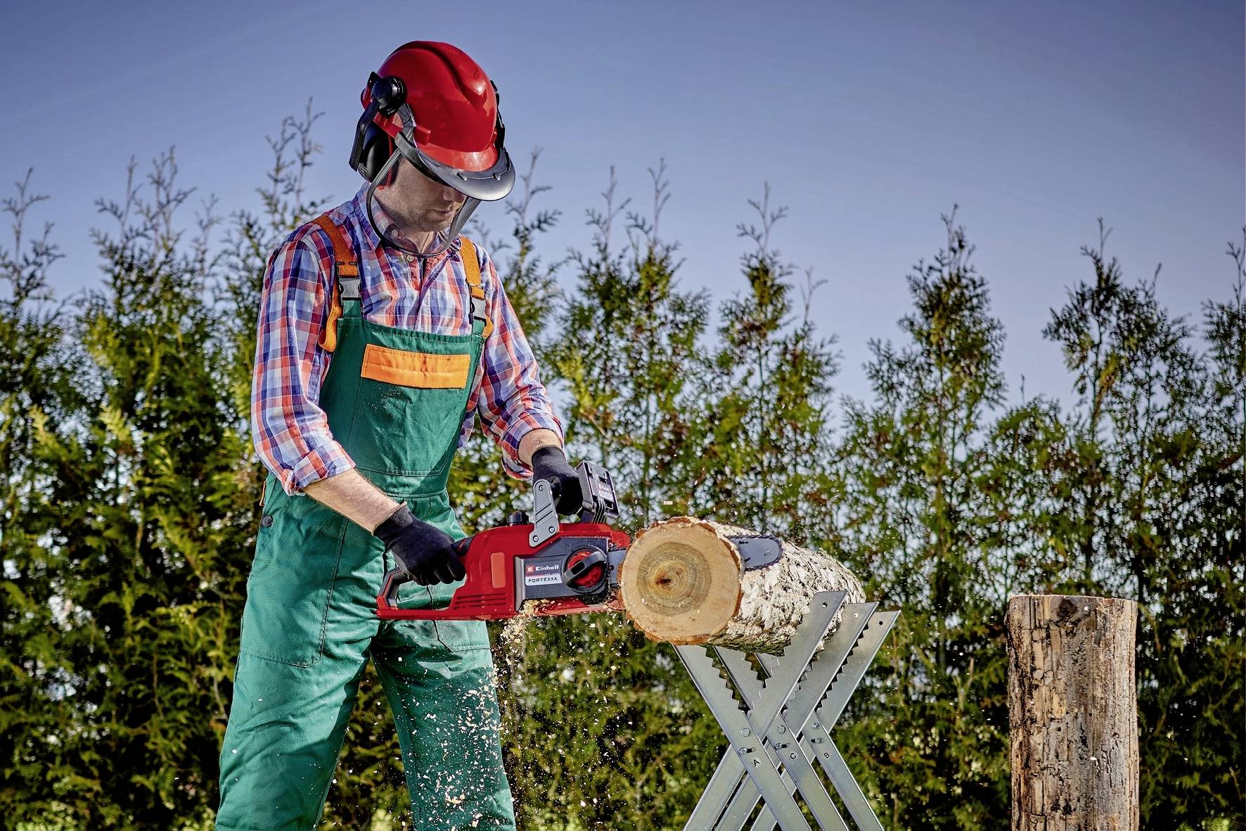 Eine Person in Schutzkleidung sägt mit einer Motorsäge Holz auf einer Arbeitsplattform im Freien.